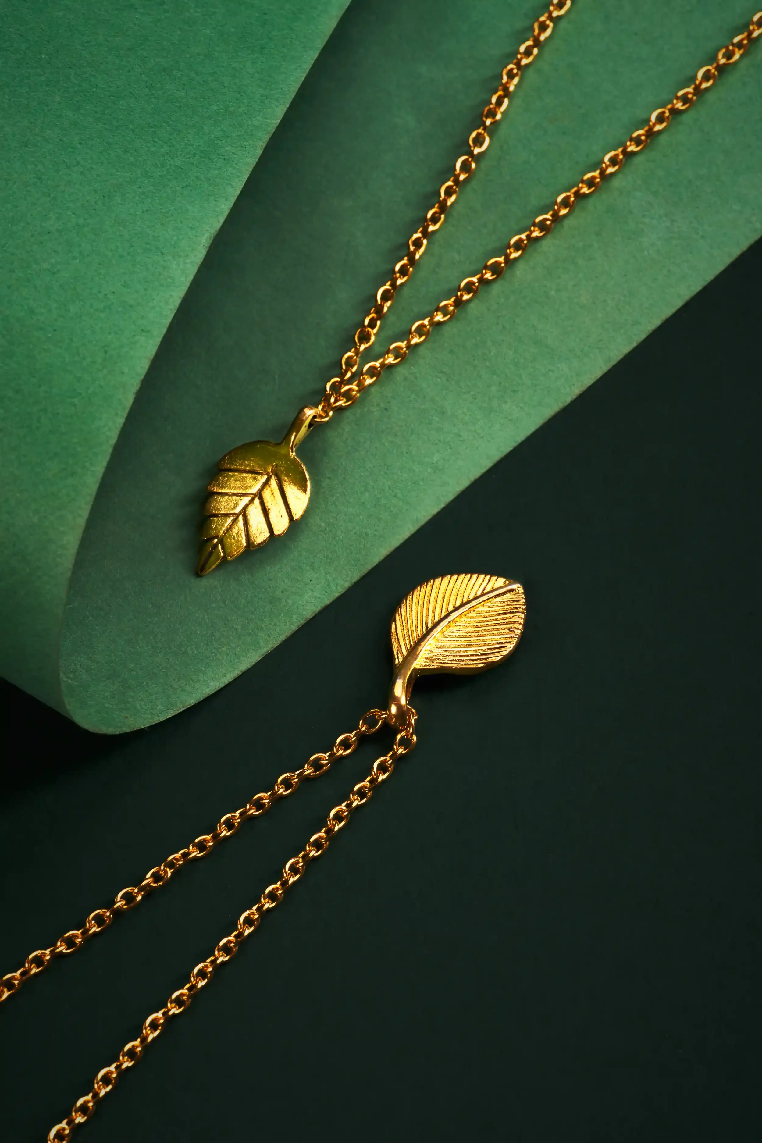 Gold leaf-shaped necklace and brooch with chain details on green background