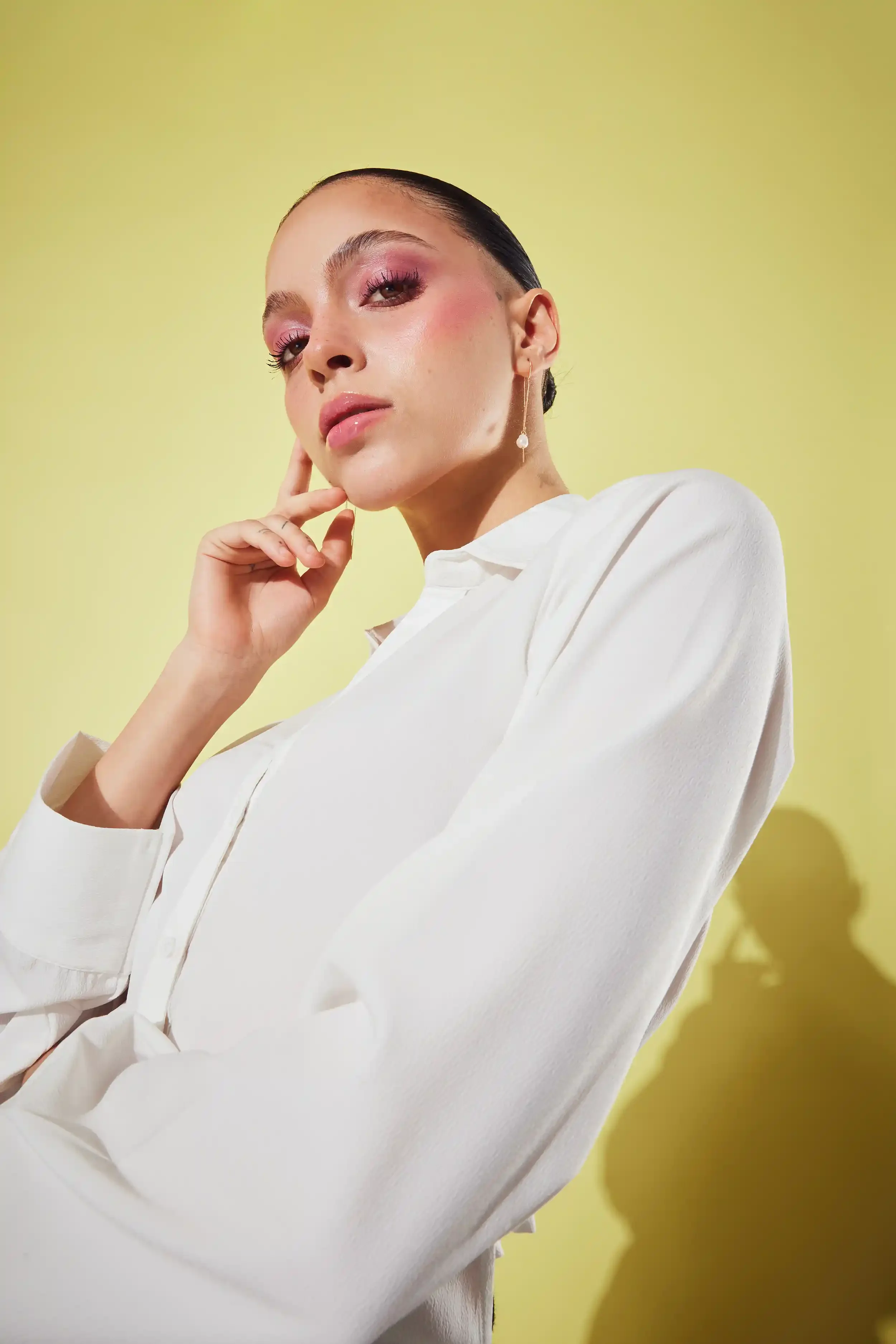 A woman with dark hair and pink makeup, wearing a white shirt, posing against a yellow background. Anandclix, Bangalore, advertising photographer, Fashion photographer, Editorial photographer, Bangalore photographer.