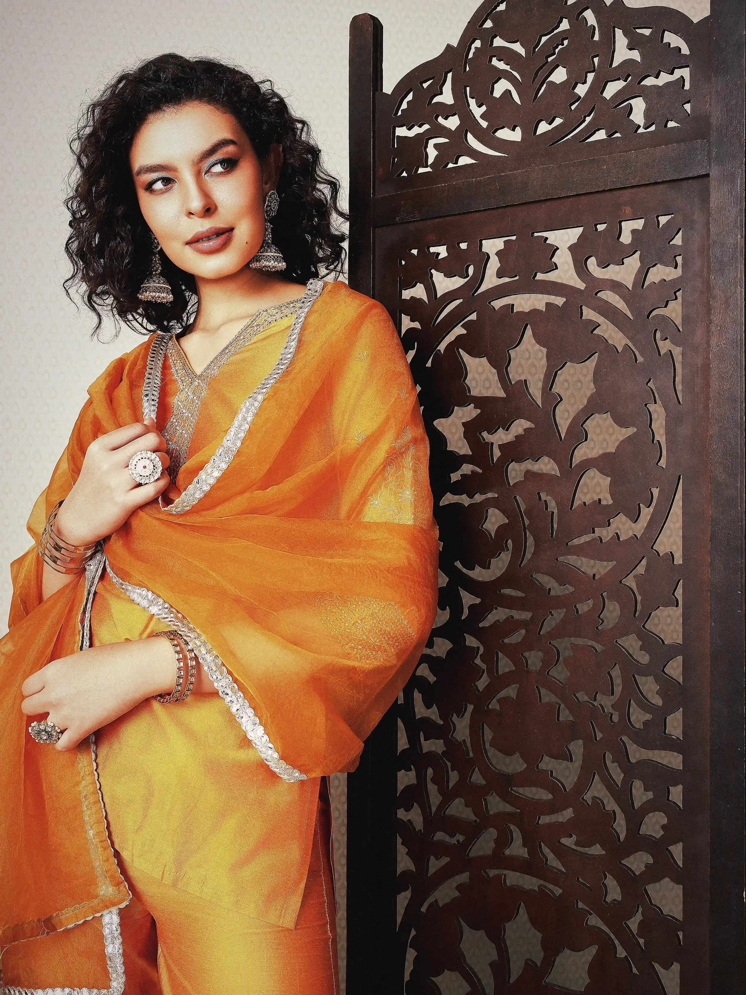 Woman wearing an orange kurta with silver embroidery, standing beside a decorative wooden screen. Anandclix, Bangalore, advertising photographer, Fashion photographer, Editorial photographer, Bangalore photographer.