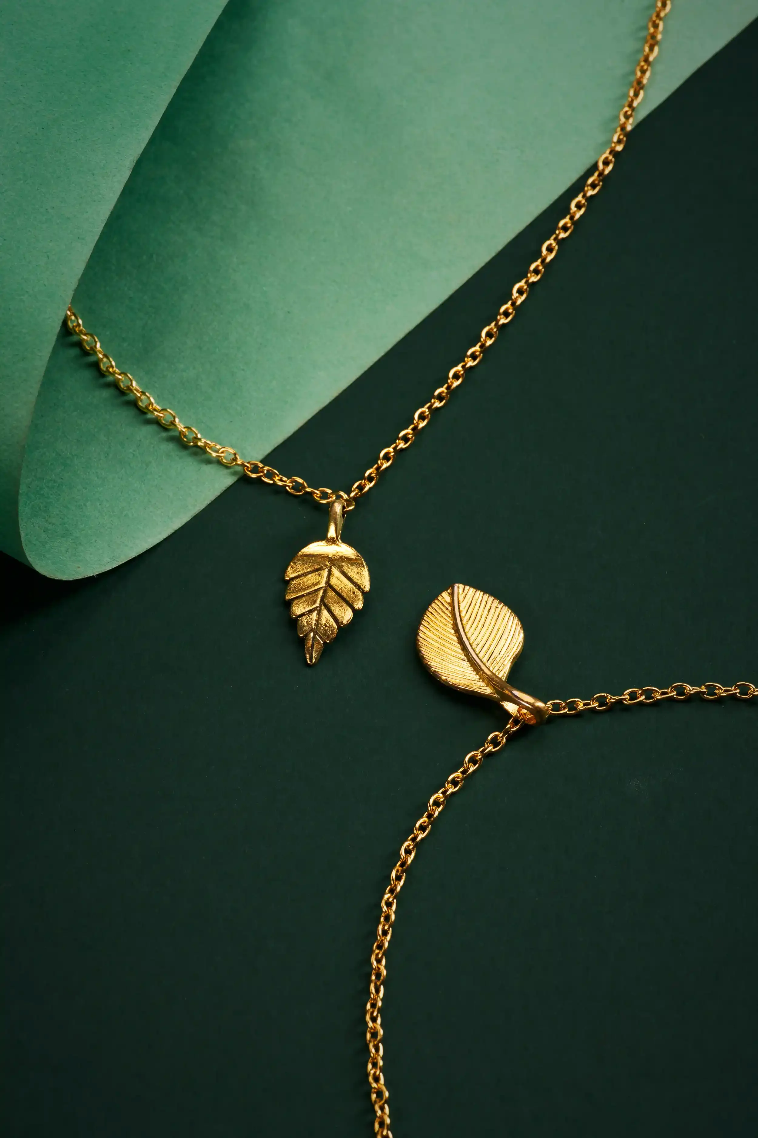 Gold leaf-shaped necklaces on a green background.