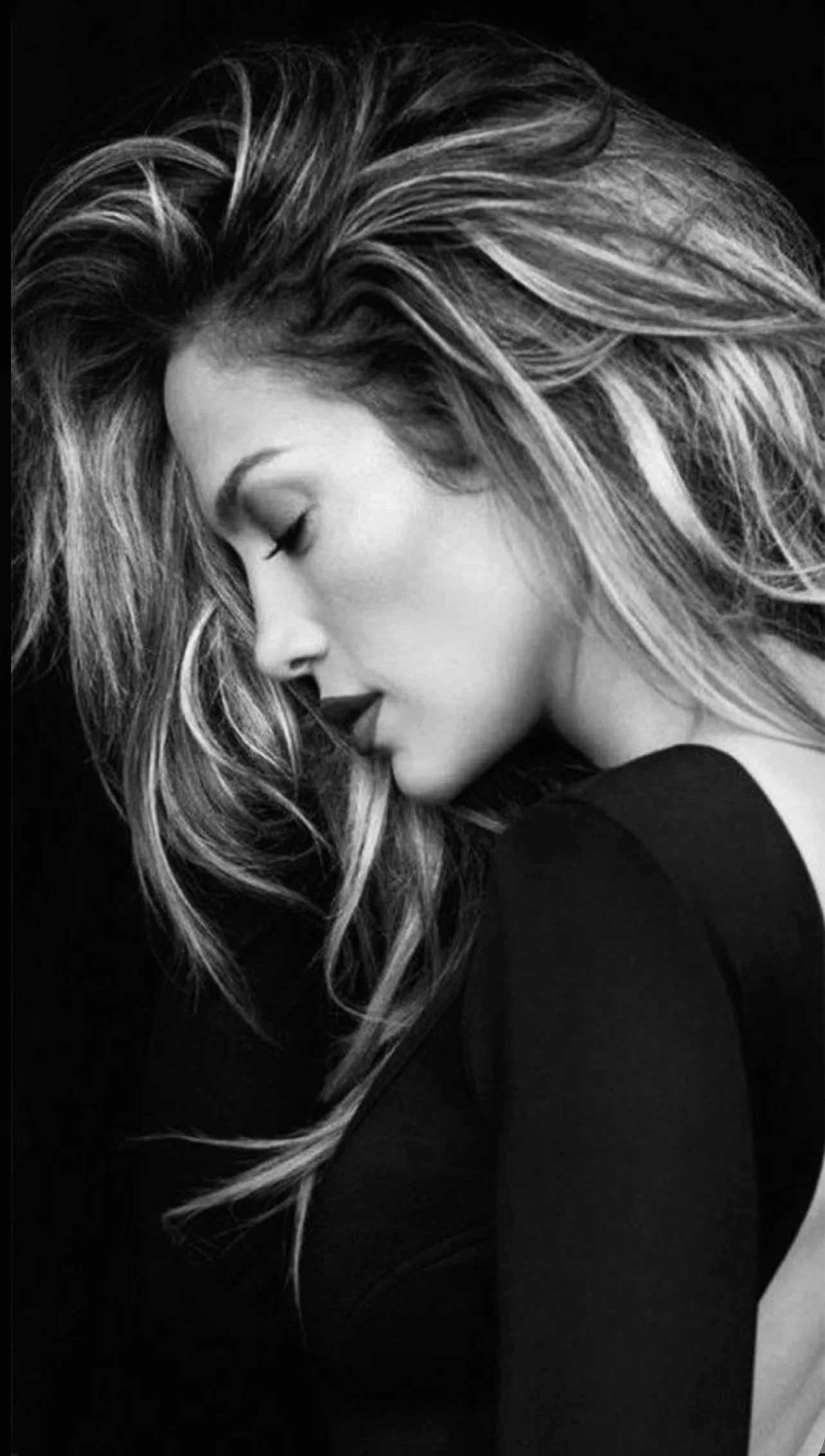 Zwarte en witte foto van een vrouw met lang, golvend haar, met haar ogen dicht en haar hoofd lichtjes naar beneden.