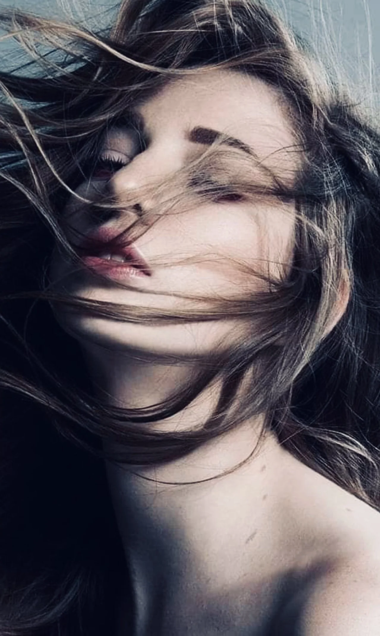 Close-up van een vrouw met lang, golvend haar die haar gezicht deels bedekt, met open ogen en lichtgekleurde lippen.