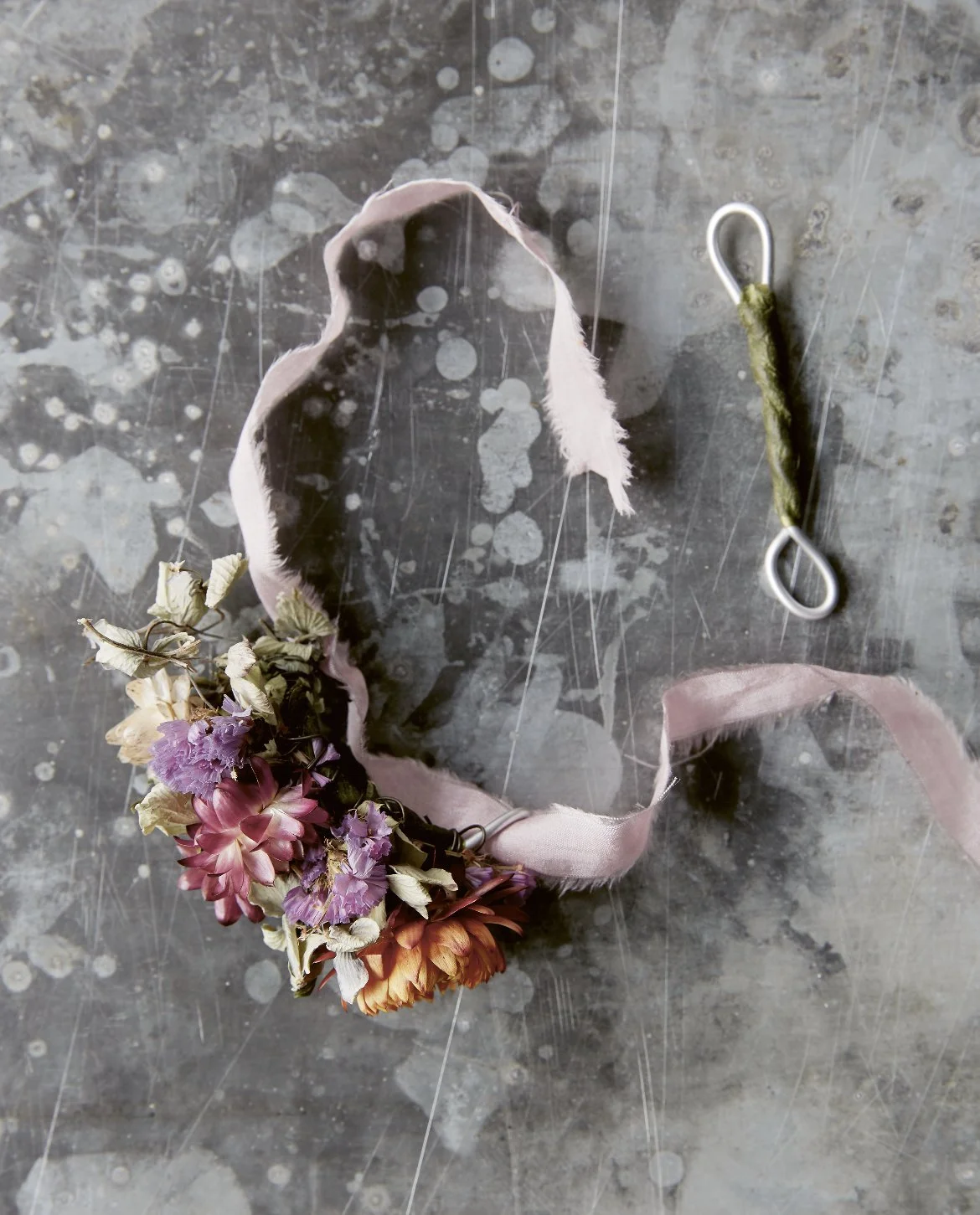 A ribbon with dried flowers attached to it, for a DIY flower crown, on a scratched concrete surface.