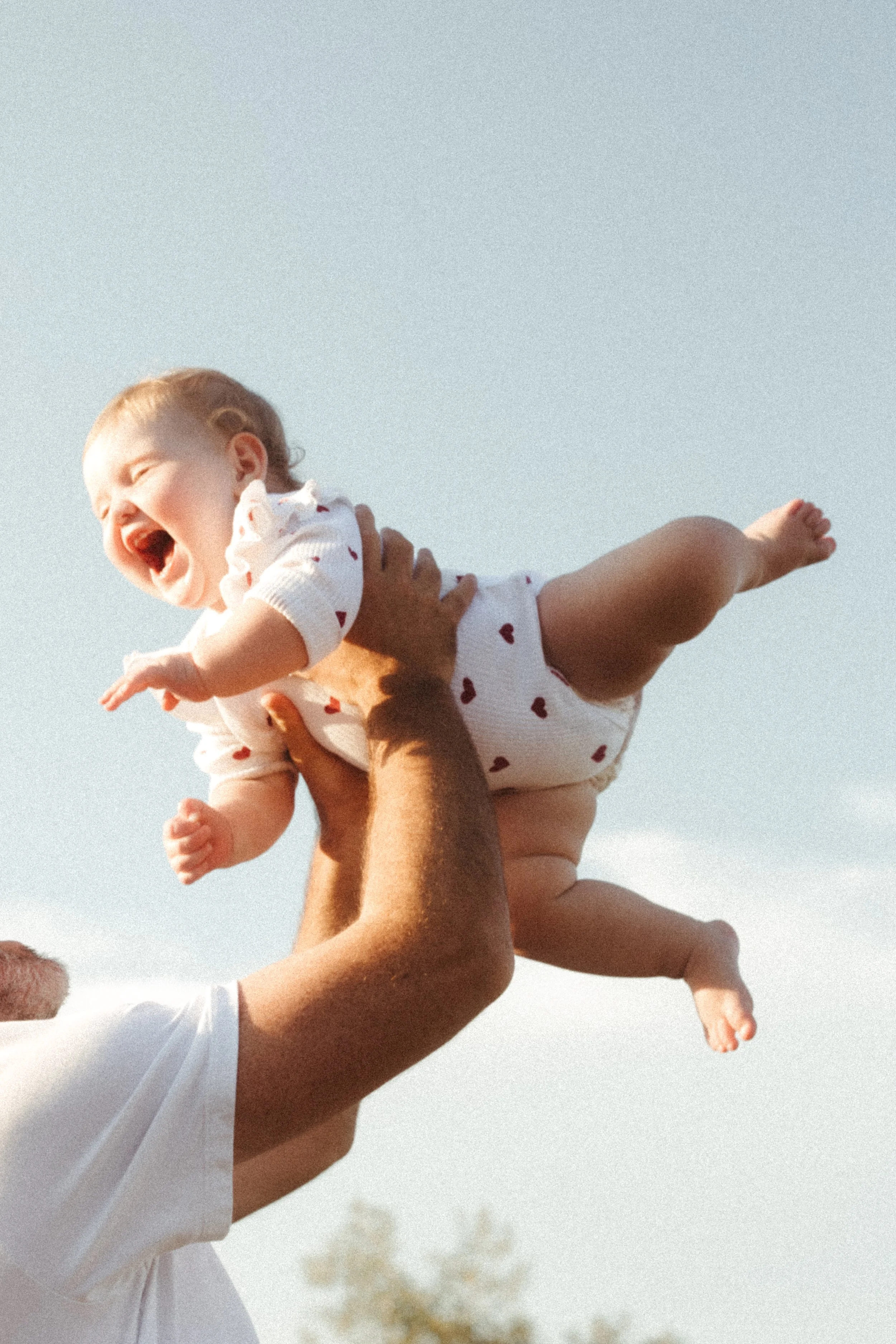 baby lifted into the air during joyful family photography session at sunset