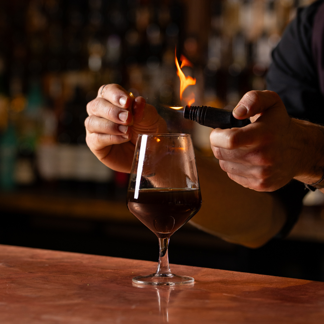 Person toasting with a glass of red wine while lighting a match with a flame.
