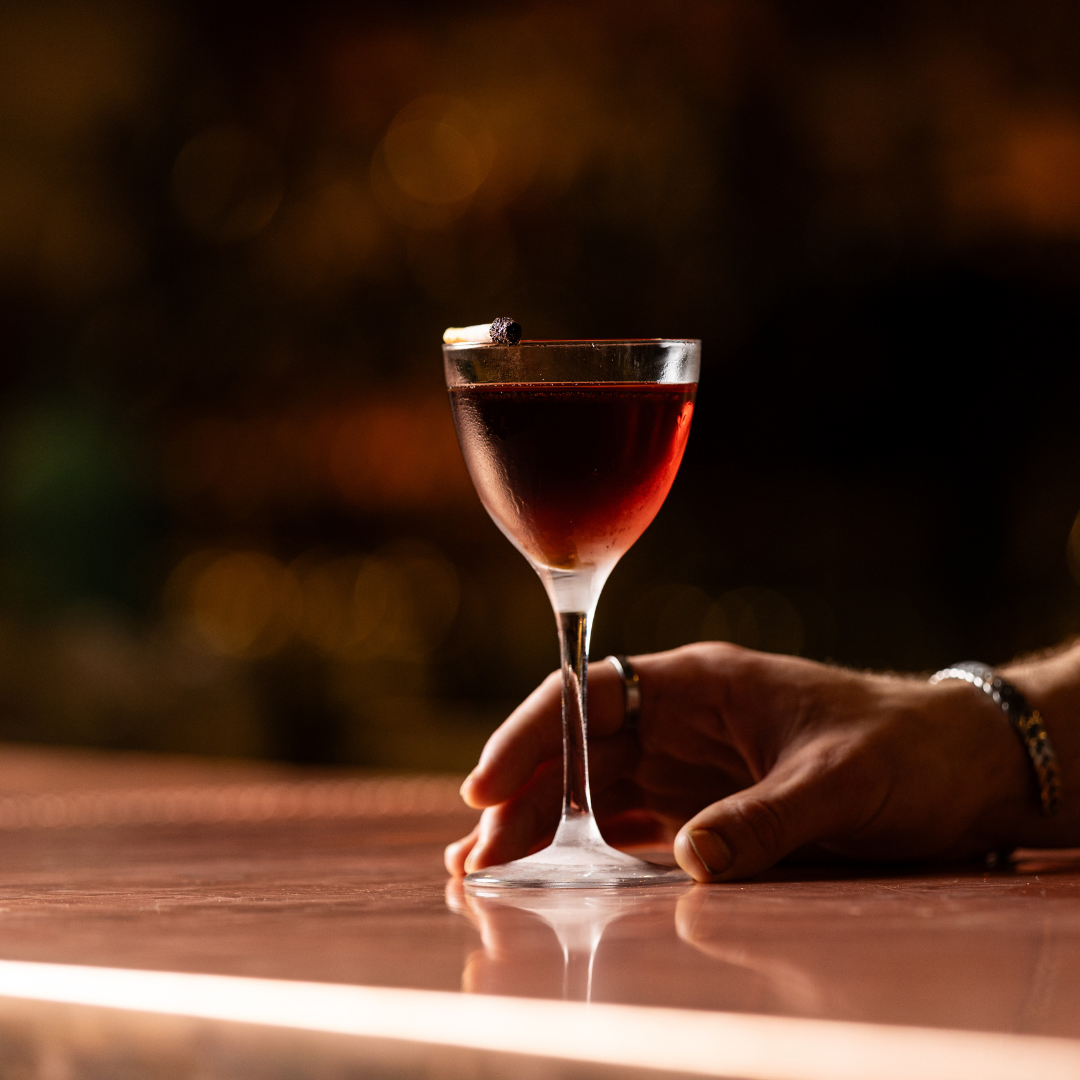A hand holding a glass of red wine with a dark, blurred background.