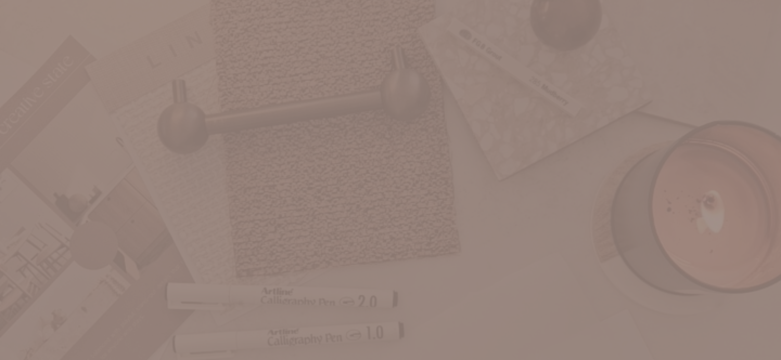 Art supplies including calligraphy pens, a textured paper, and a pen holder on a desk.