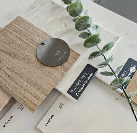 Close-up of material boards including a plant with green leaves, tapware finishes in gunmetal by ABI interiors, and some cabinetry finishes samples.