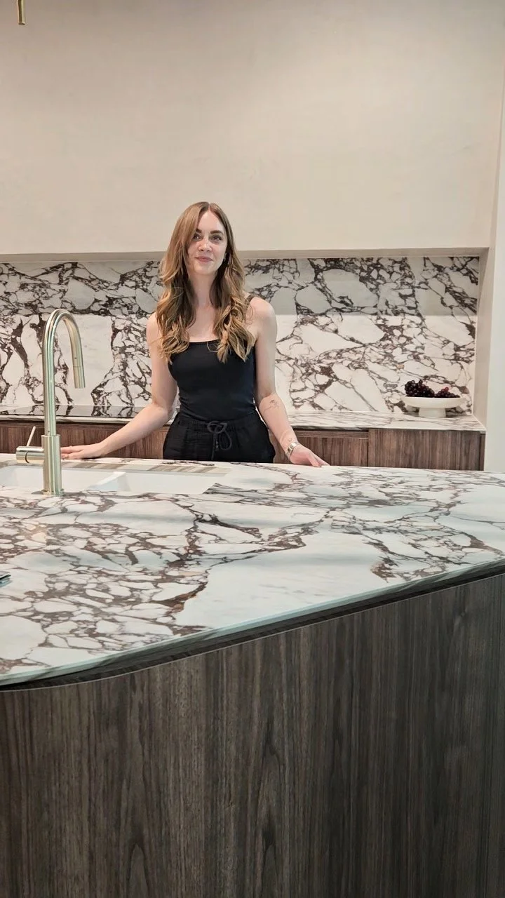 Vanessa standing behind a marble kitchen island with a marble backsplash, in a modern kitchen. This picture was taken at Homebase in Subiaco, Western Australia.