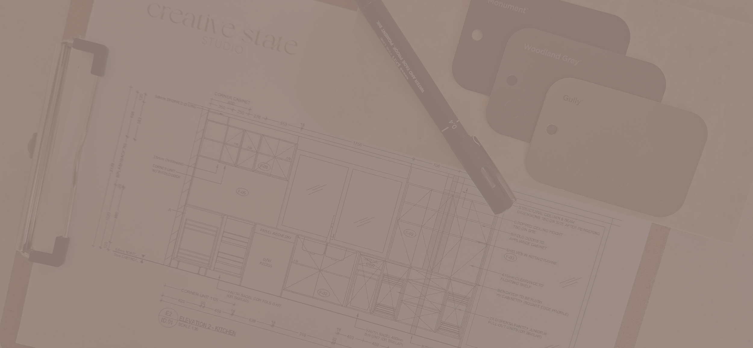 Floor plan drawing, a pen, color samples labeled "Woodland Grey" and "Gully," and a metal ruler on a desk.