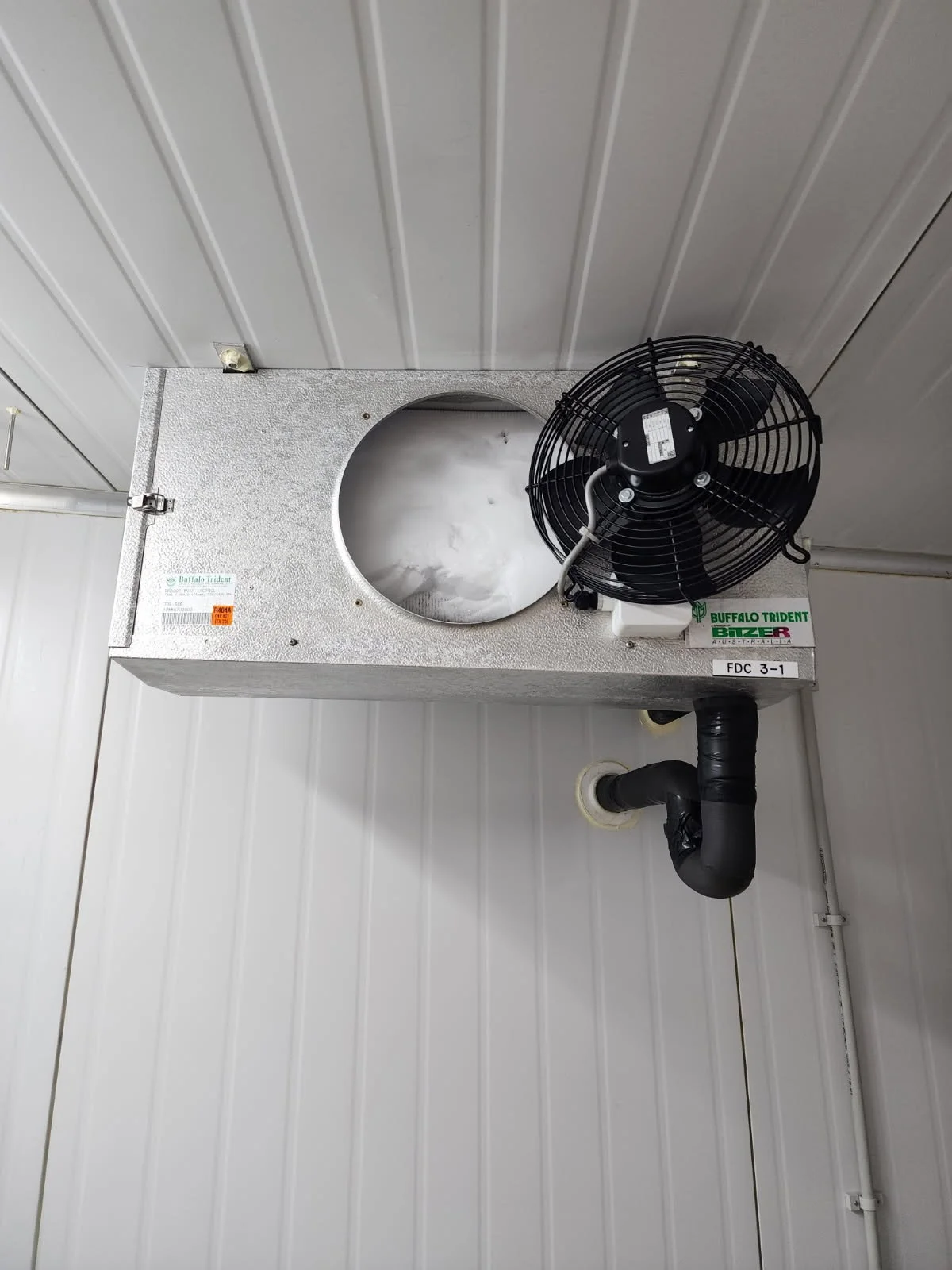HVAC unit or cooling system installed on a metal ceiling with a black fan and a pipe connected to it.