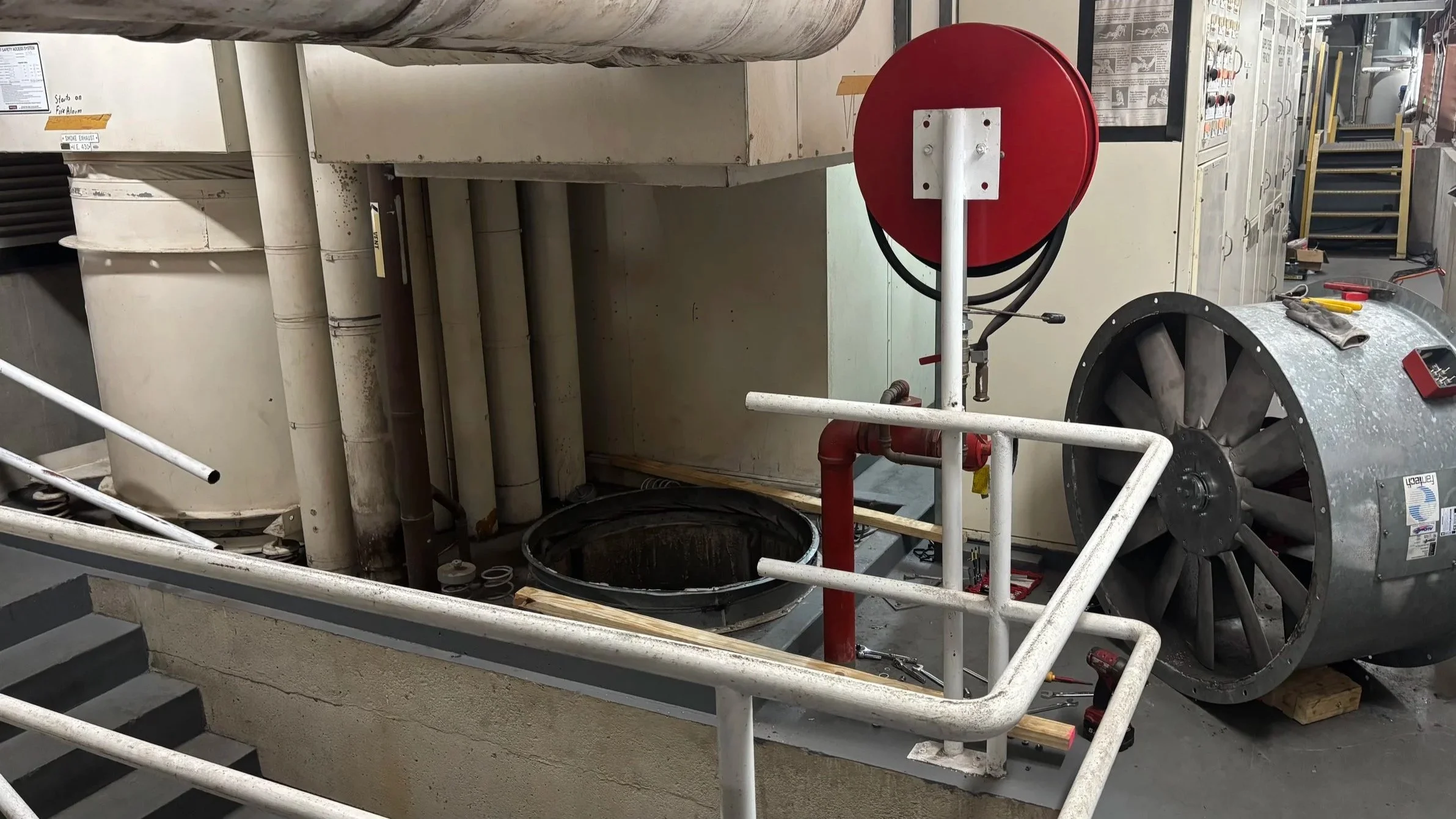 Industrial cleaning or maintenance equipment near a large ventilation fan and pipes in a commercial or industrial setting.