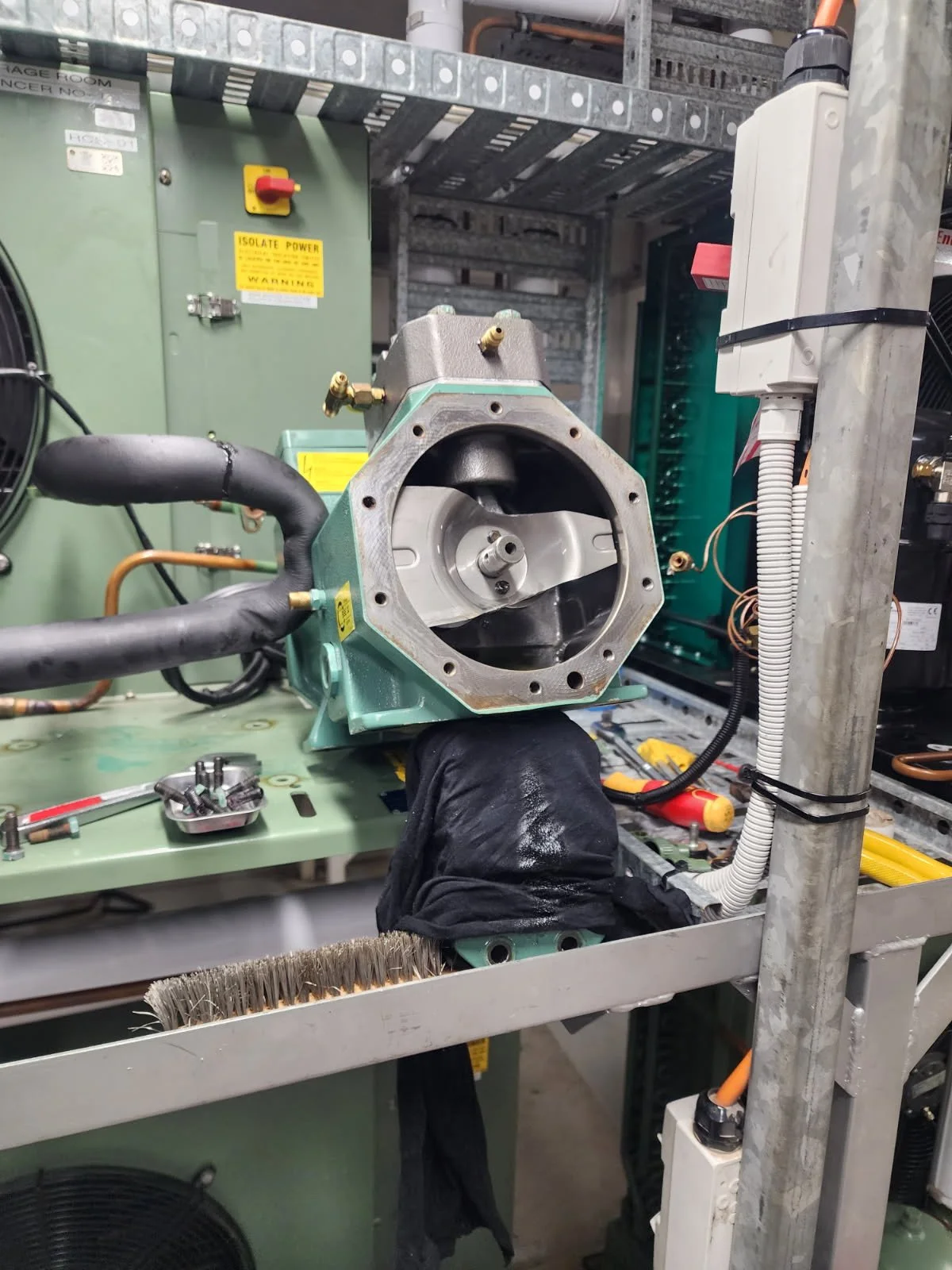 A person working with a machine part in an industrial setting, with tools and electrical panels visible in the background.