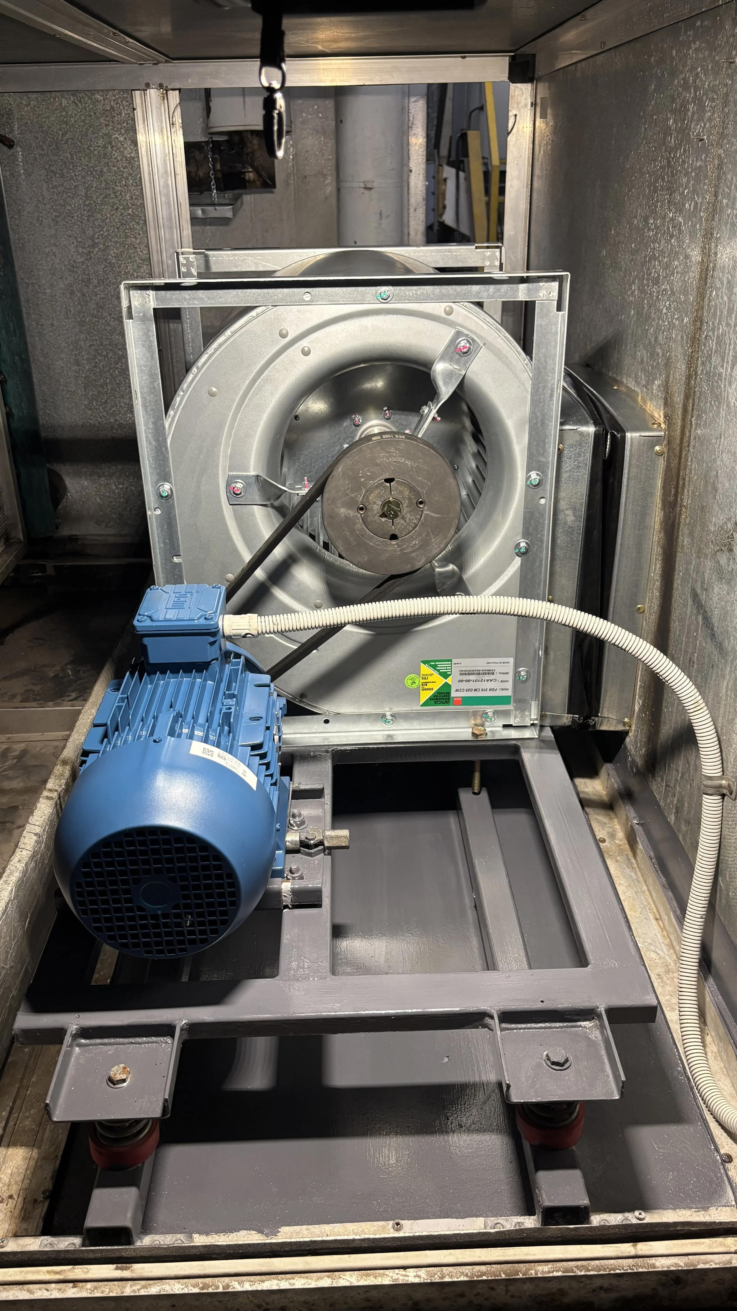 Industrial machine with a blue motor, metal frame, and large circular component, situated inside an industrial setting.