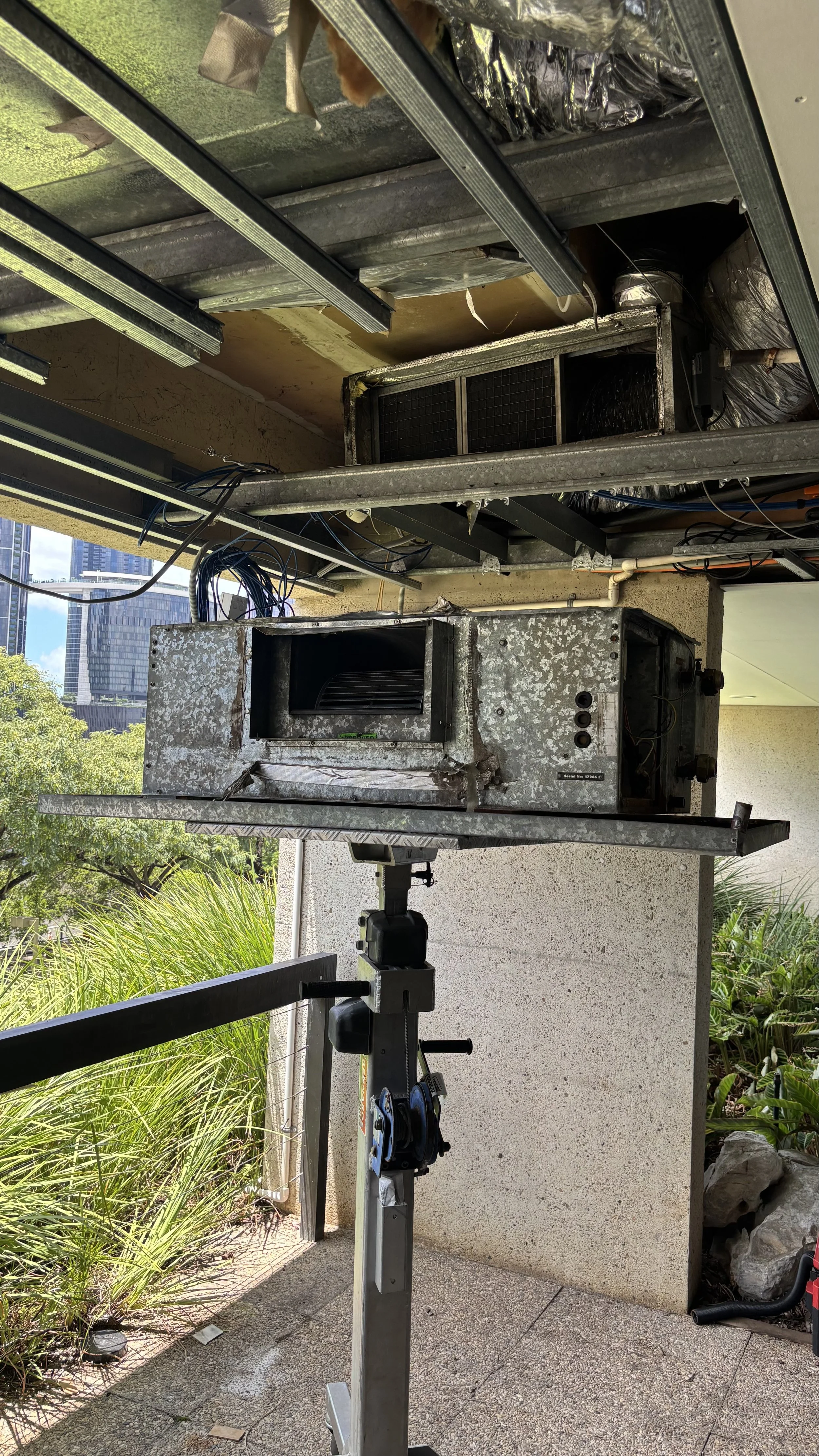 Deconstructed commercial oven or stove with exposed heating elements, mounted on a stand on an outdoor balcony with plants and city buildings in the background.