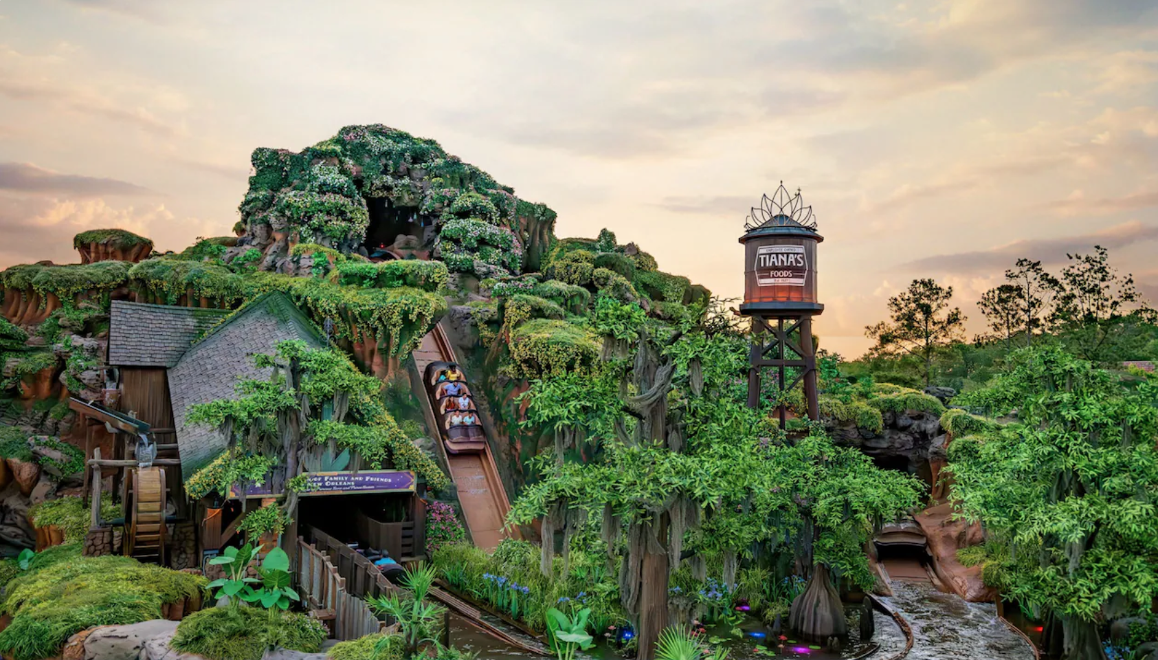 A lush theme park with a jungle and mountain landscape, featuring water slides, greenery, and a water tower labeled 'Tiana's Foods' at sunset.