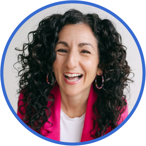 A woman with curly black hair and hoop earrings smiling and winking, wearing a pink blazer over a white shirt.