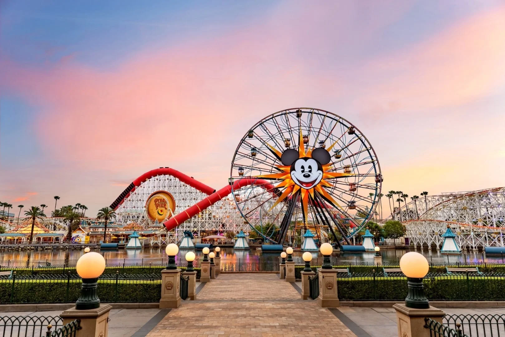 Disney California Adventure Park at sunset with Mickey Mouse face Ferris wheel and roller coaster
