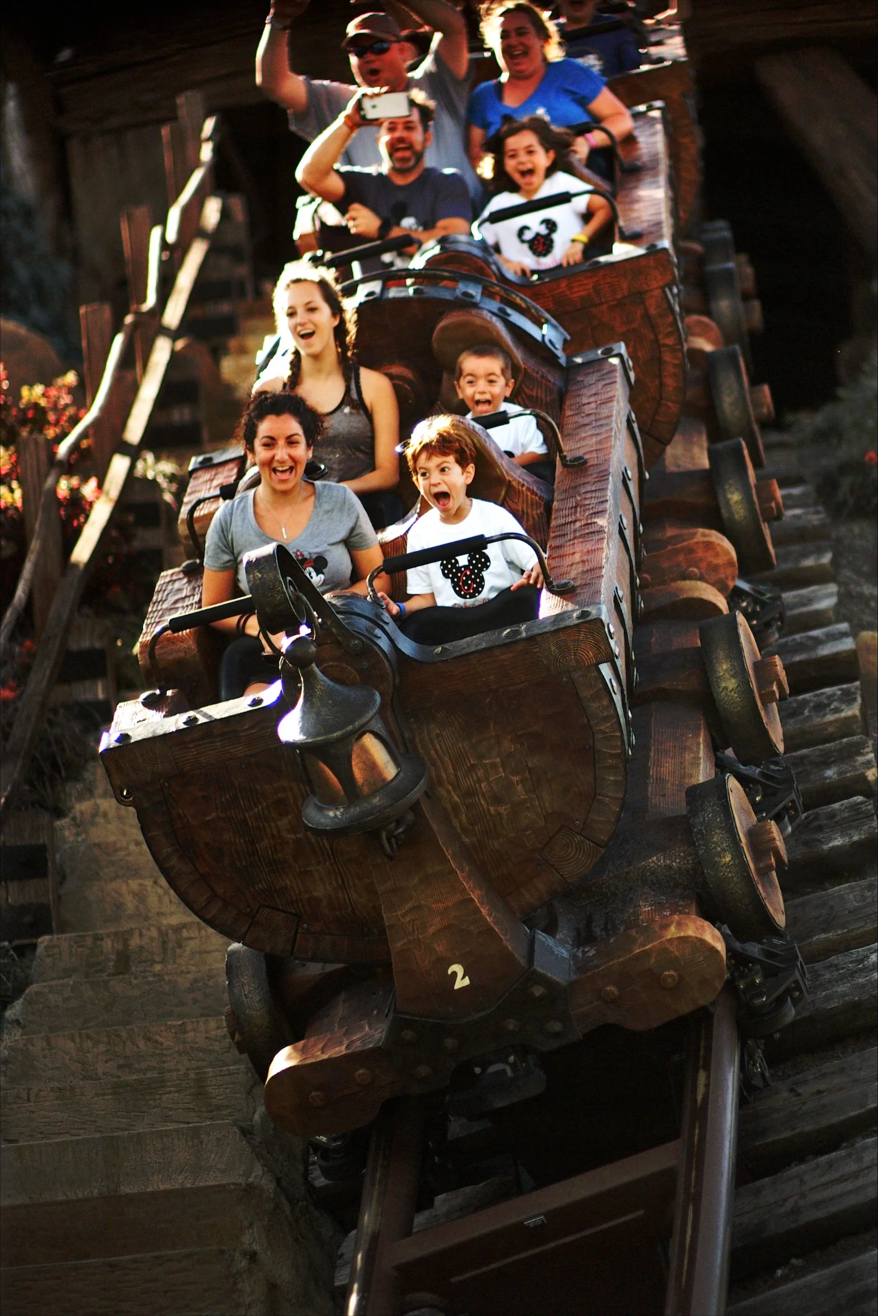 A group of people riding a wooden roller coaster at an amusement park, excited and joyful.