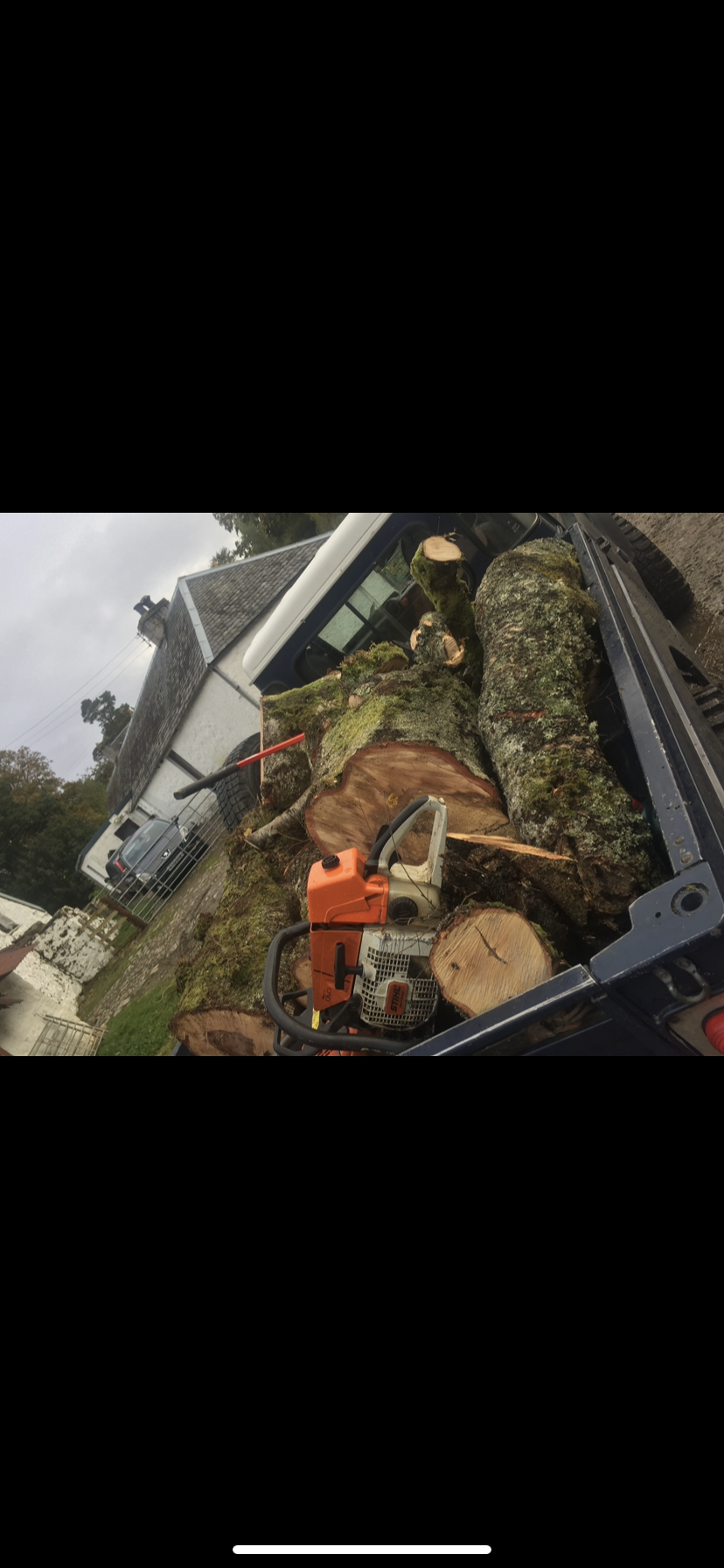 A truck bed filled with cut tree logs, a chainsaw, and a garden rake, outdoors in a residential area during daytime. Firewood and Timber Inverness.