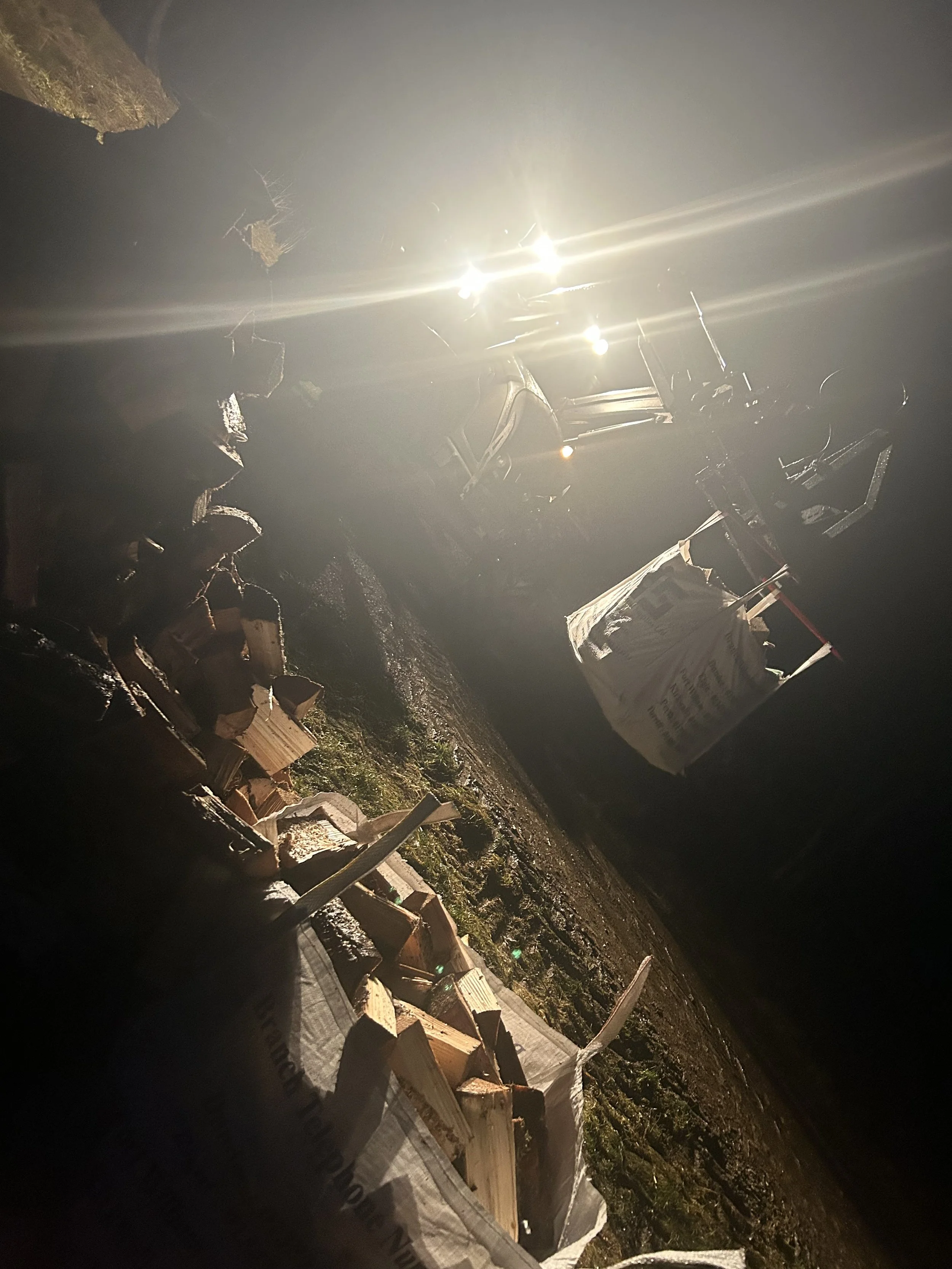 Construction site at night with wooden planks, a small white truck, and construction materials illuminated by bright sunlight. Firewood Aviemore.