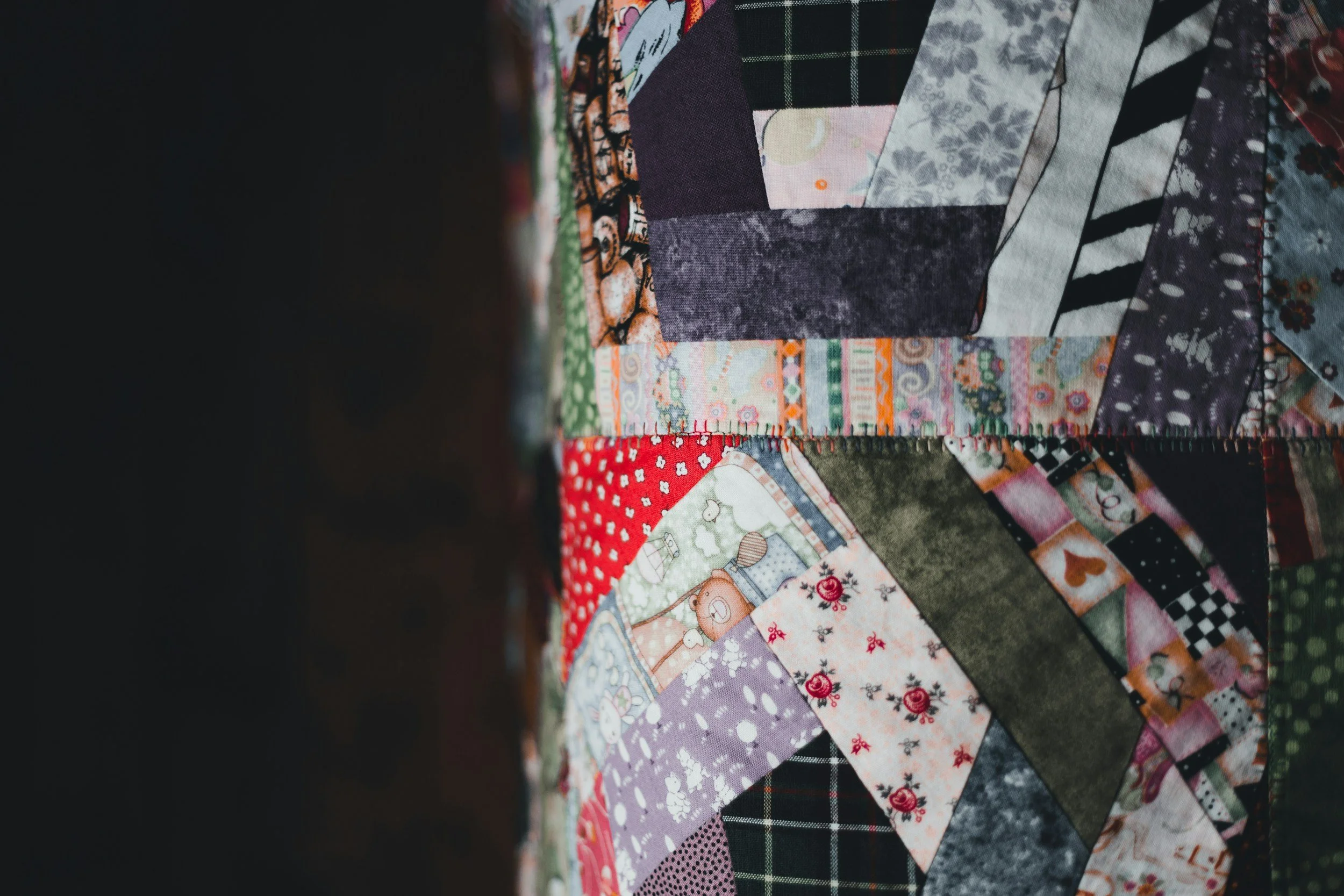 Close-up of a colorful quilt with various patterned fabric pieces, including floral, checkered, and polka dot designs.