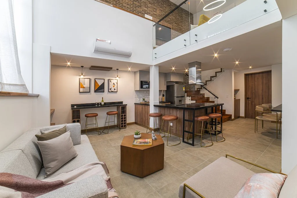 Open-concept living room and kitchen with modern decor, bar stools, staircase, and loft area.