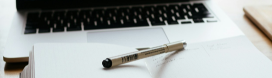 Open laptop, notebook, and pen on desk.