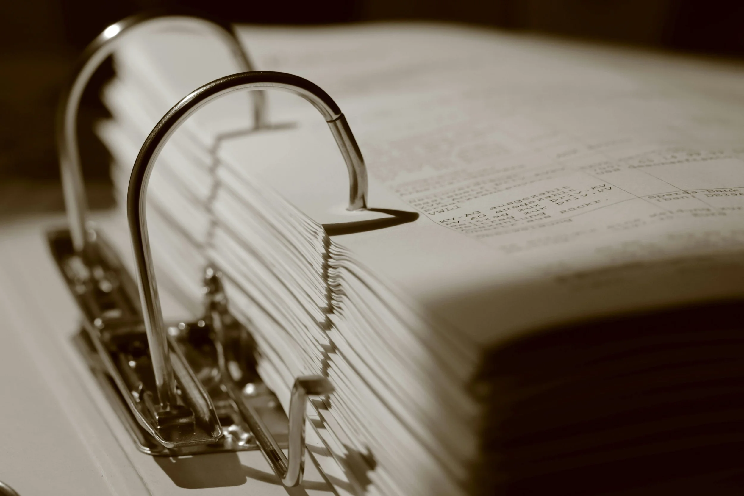 Close-up of a ring binder with paper inside, showing metal rings and pages with printed text.