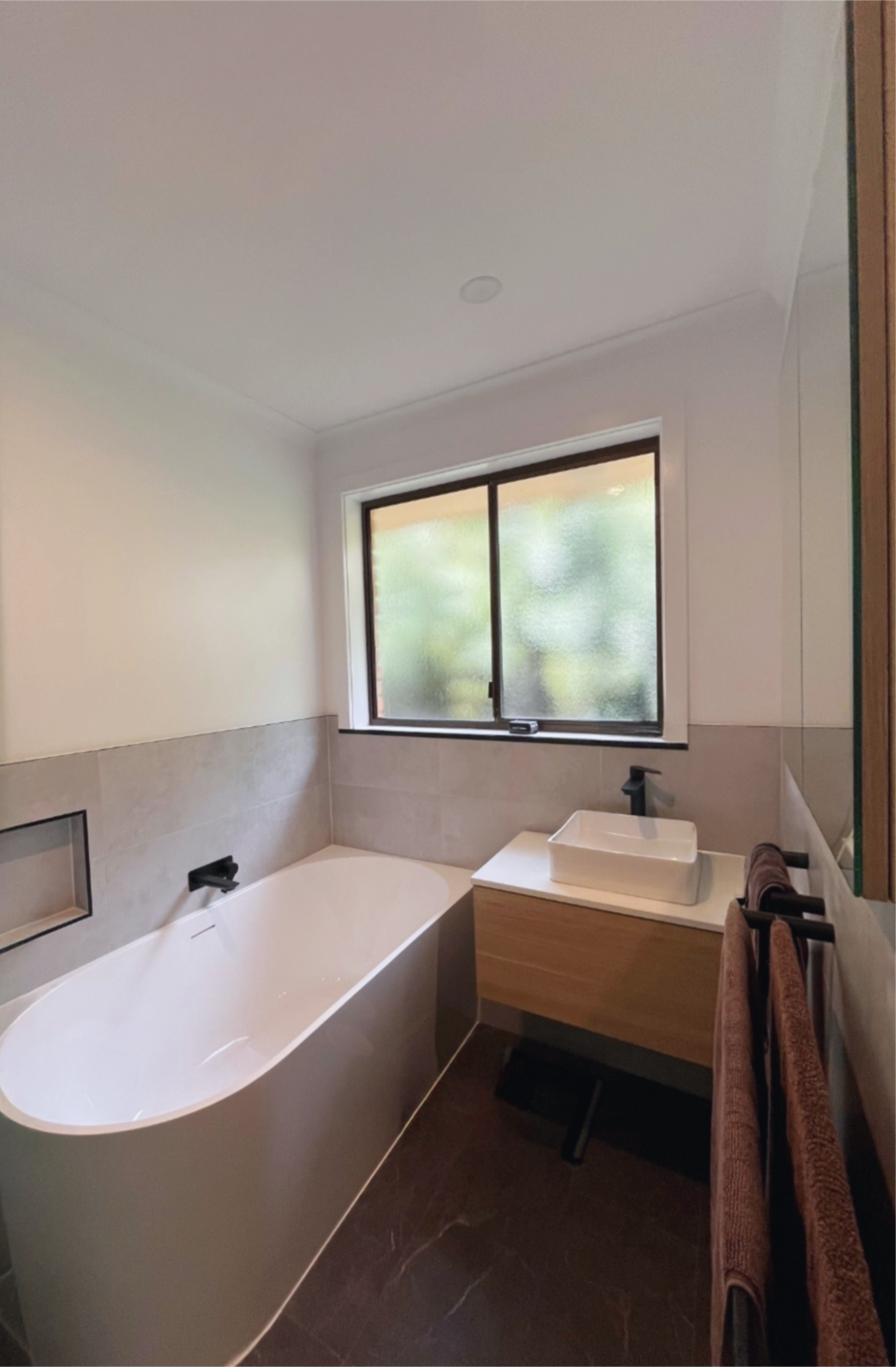 Bathroom with a bathtub, a window, a sink, and towels hanging on a rack.