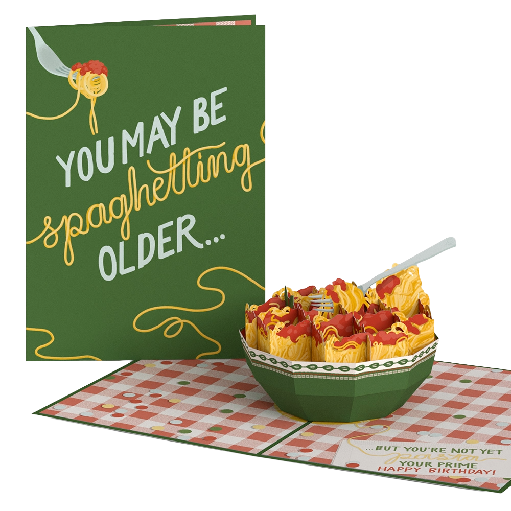 A birthday card with the message 'You may be spaghettizing older... but you're not yet your prime. Happy birthday!' and a bowl of spaghetti with meat sauce. A fork is piercing some spaghetti in the bowl, which is set on a red and white checkered tablecloth.