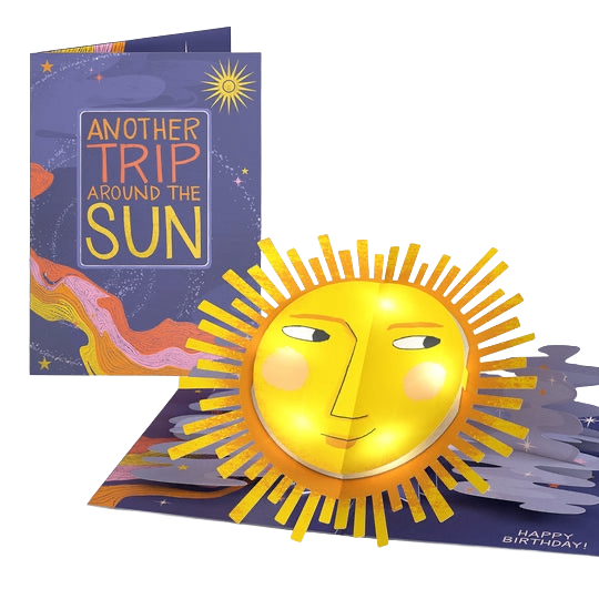 A colorful birthday pop-up card featuring a smiling sun with a face and rays, and a the card cover with the title 'Another Trip Around the Sun' and a sun illustration in the background.