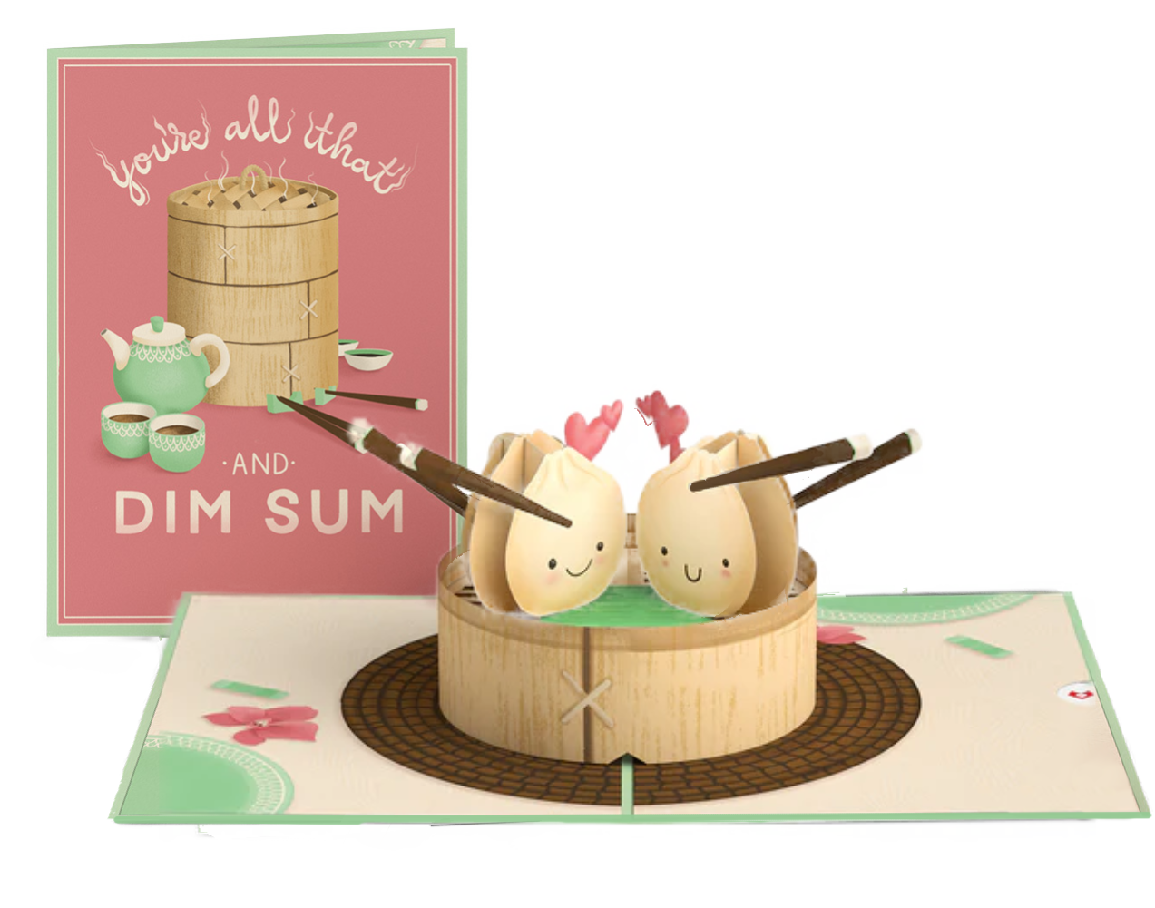 A pop-up greeting card featuring a bamboo steamer, a teapot, and teacups, with two dumplings with smiling faces and chopsticks, set on a decorative base with pink heart-shaped accents.