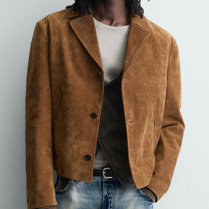 Person wearing a brown suede jacket over a gray t-shirt and layered with a black cardigan, with jeans.