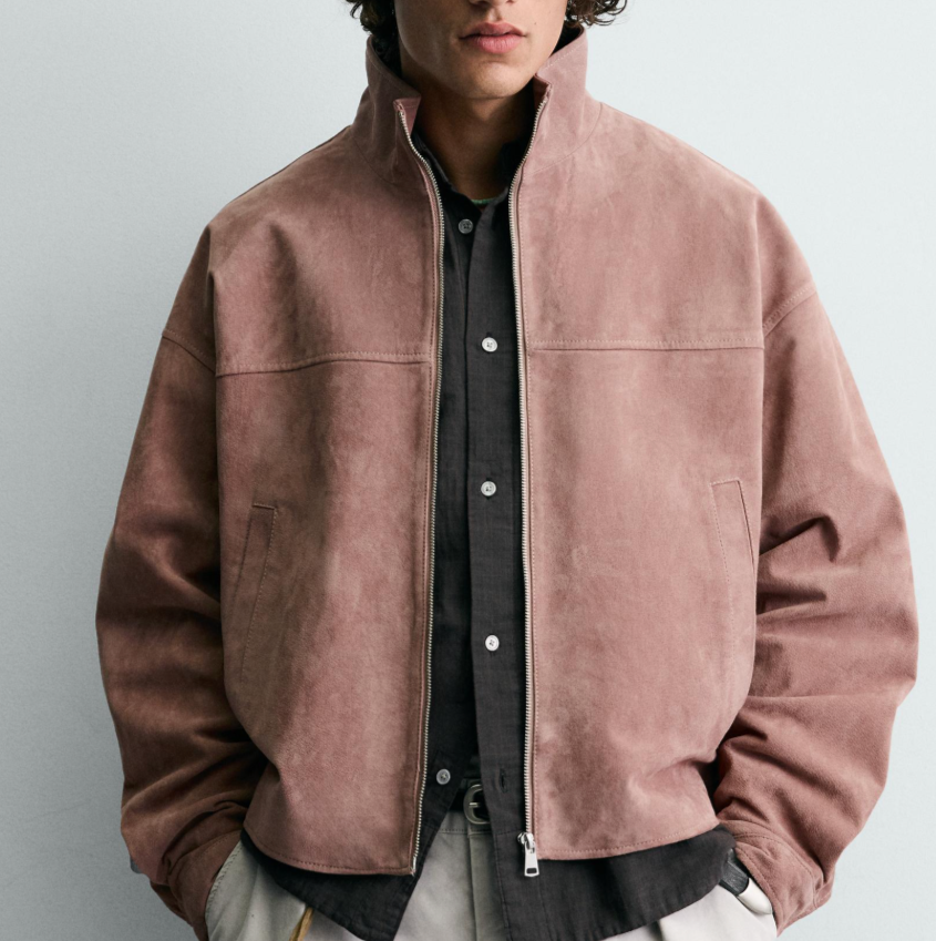 Man wearing a pinkish suede jacket over a black button-up shirt, standing against a light background.