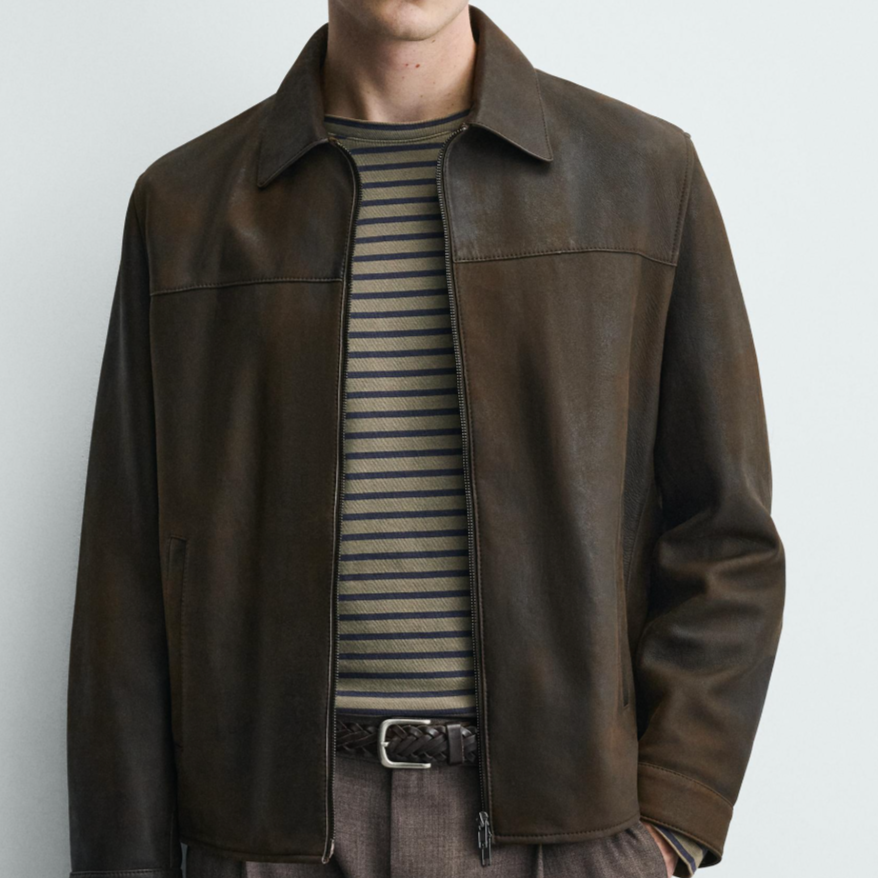 A man wearing a brown leather jacket over a striped shirt, with gray pants and a belt.