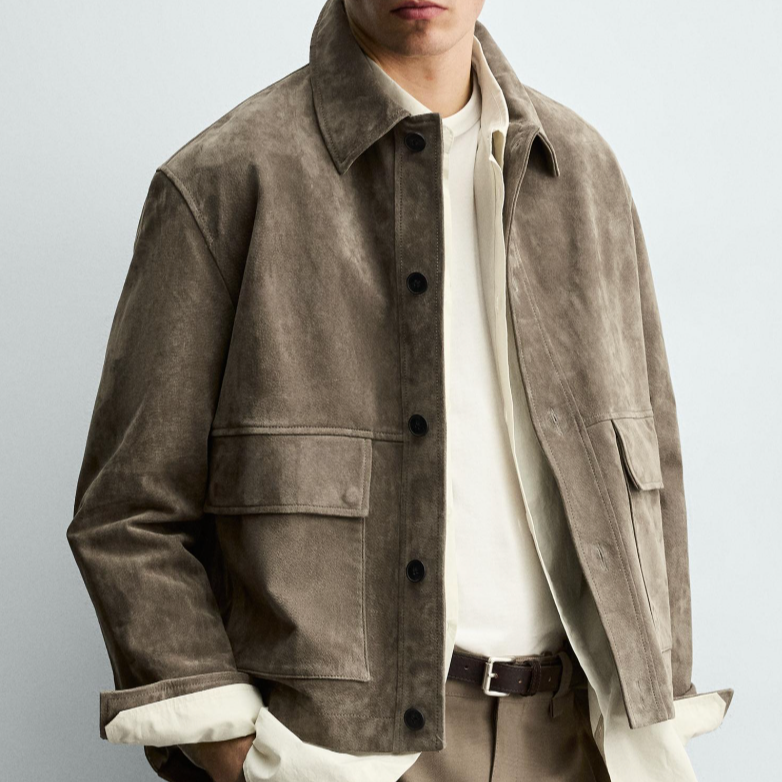 A man wearing a beige suede jacket over a cream shirt, with beige trousers and a dark belt.