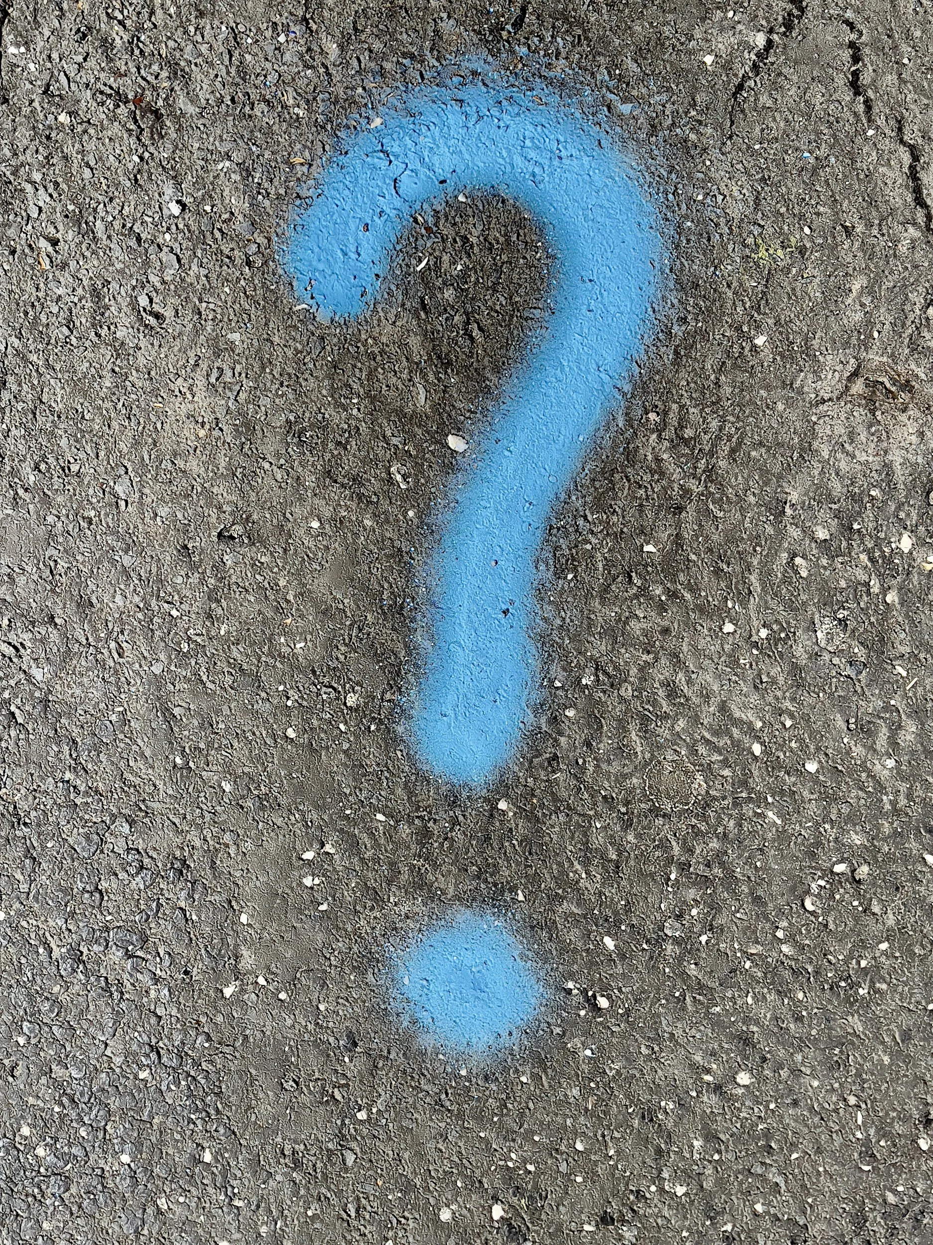 Blauwe graffiti in de vorm van een vraagteken op de grijze stoep.