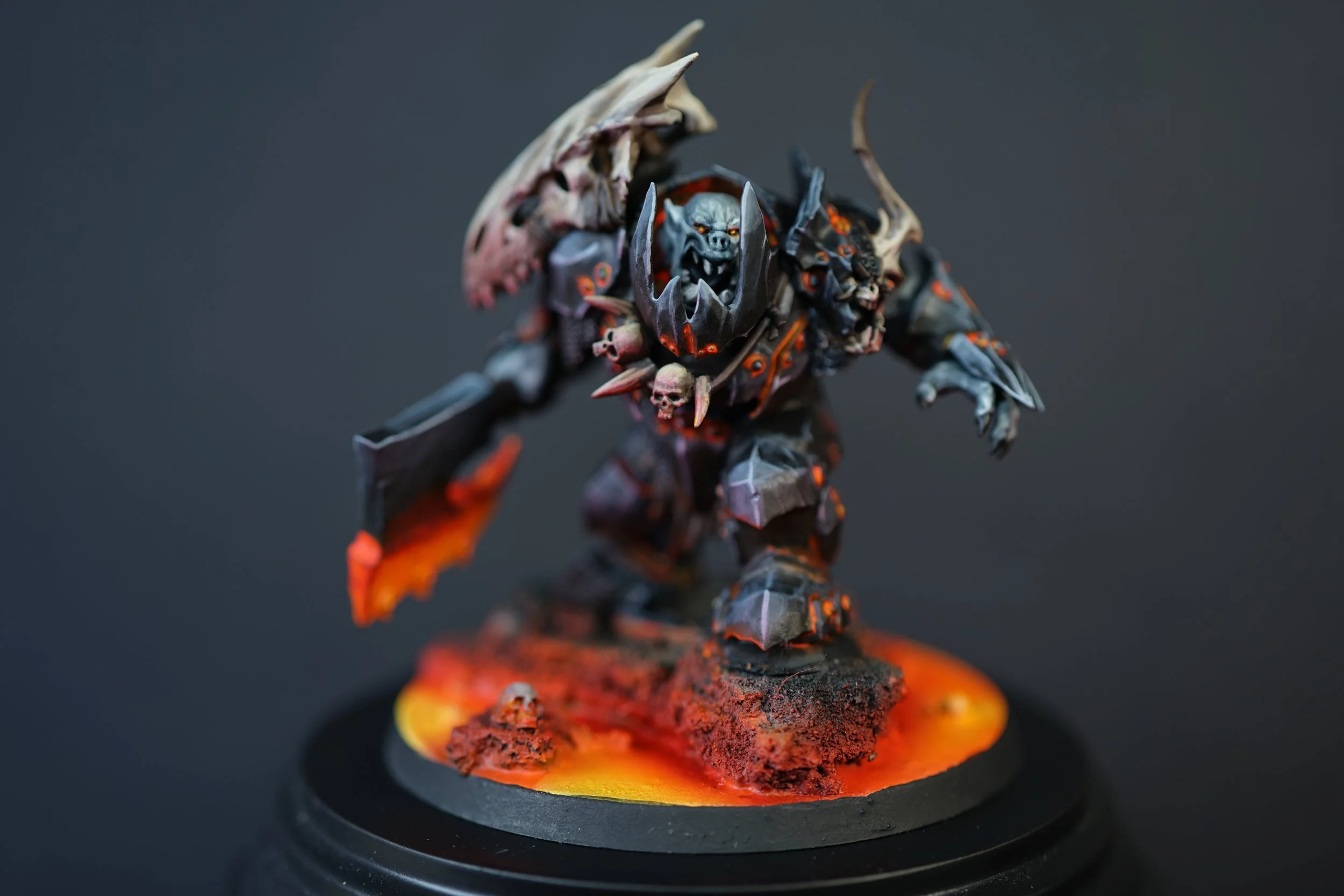 A painted miniature figure of a fearsome Orruk warrior from Warhammer Age of Sigmar with bones and spikes, standing on a base with fiery orange and red colors.