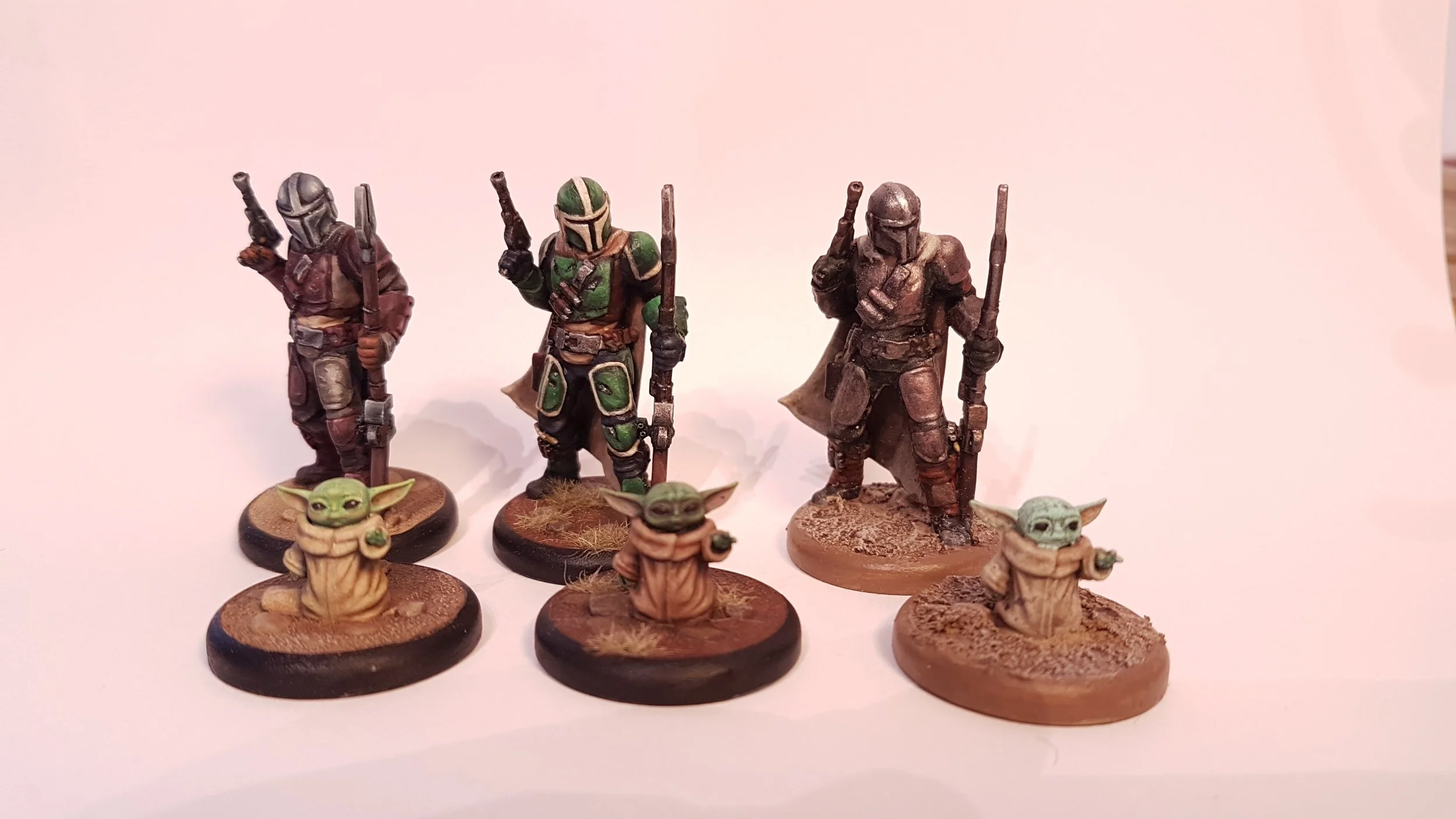 Collection of miniature figurines from Star Wars featuring three Mandalorian warriors and three Baby Yoda characters on textured bases.