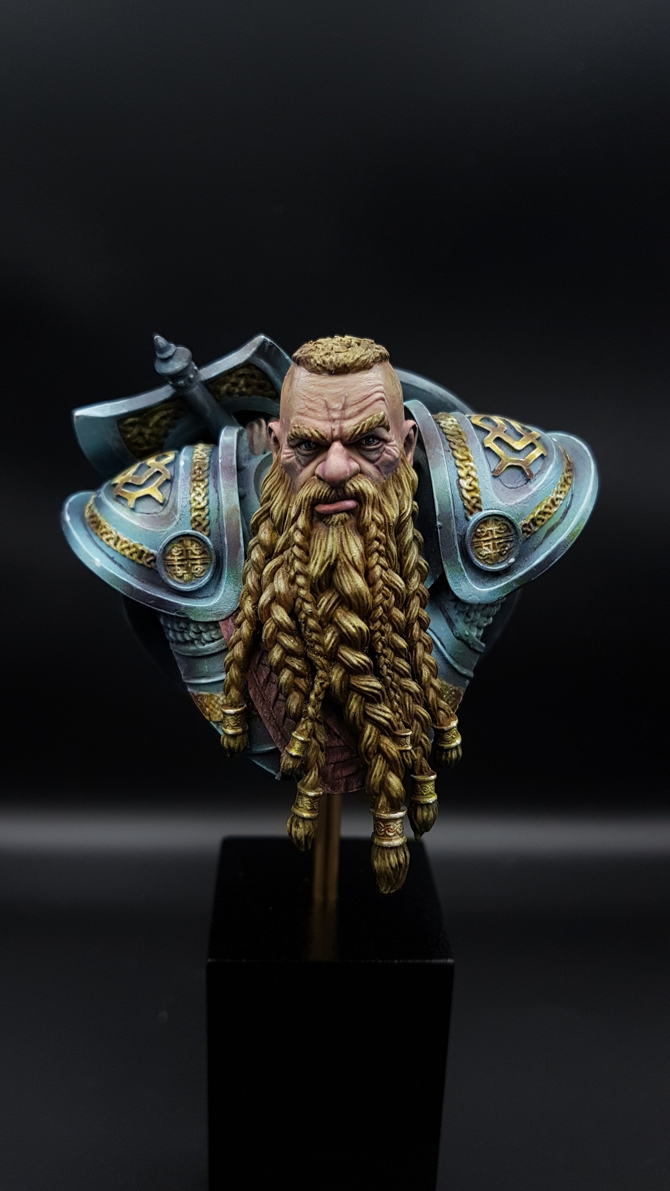 A detailed miniature bust of a dwarf warrior with long braided blond hair and beard, wearing ornate armor with gold accents, against a black background.