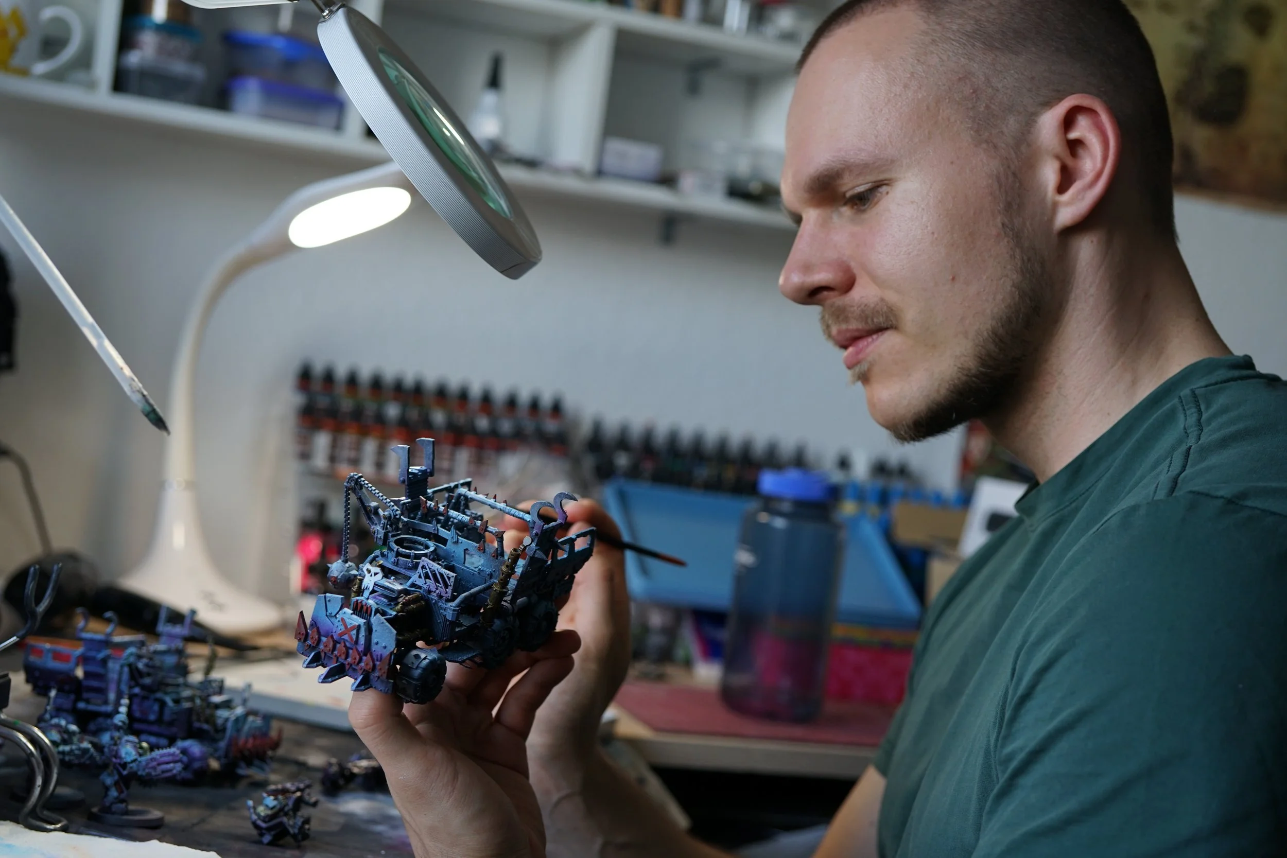 A man examining a detailed miniature model on his workbench in a workshop or hobby space.