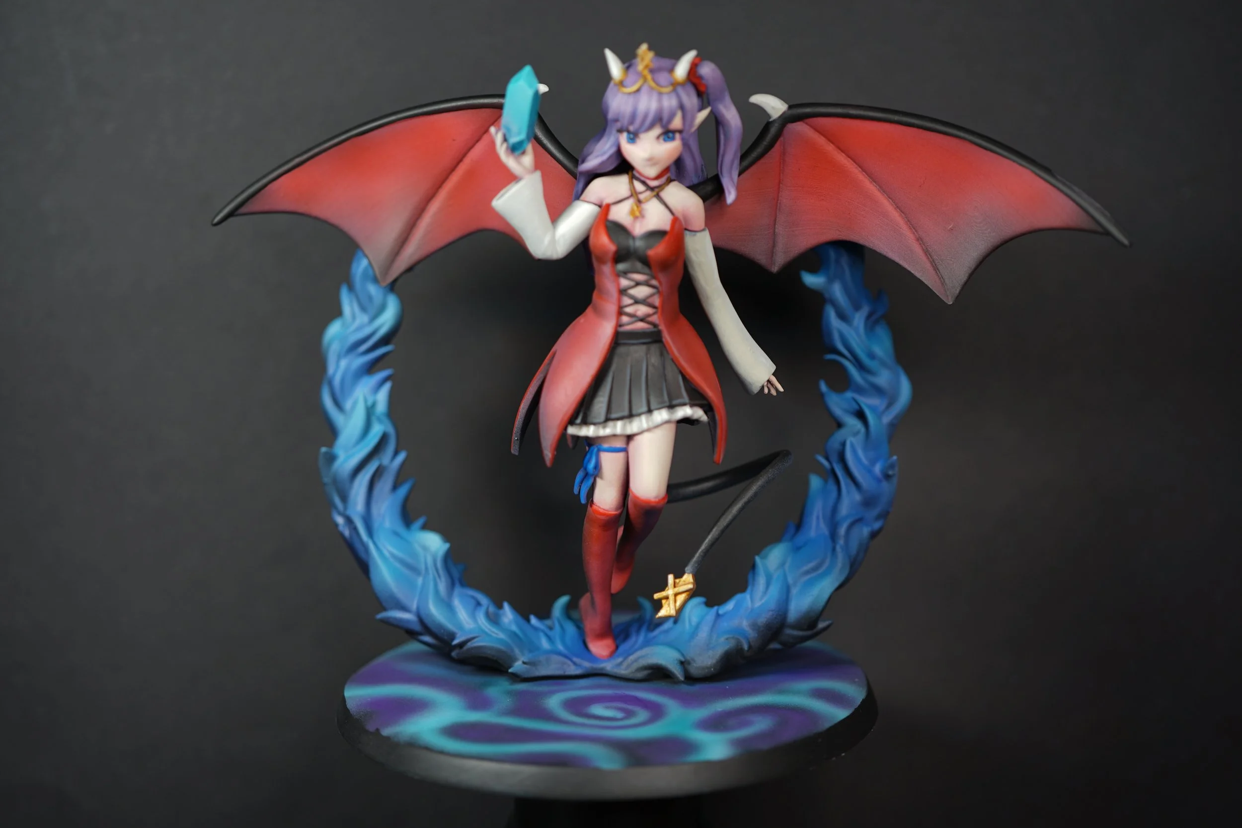 Anime-style figurine of a female character with purple hair, horns, and bat-like wings, dressed in a red and black dress with long gloves, standing on a circular base with blue swirling patterns, surrounded by blue flame-like effects.