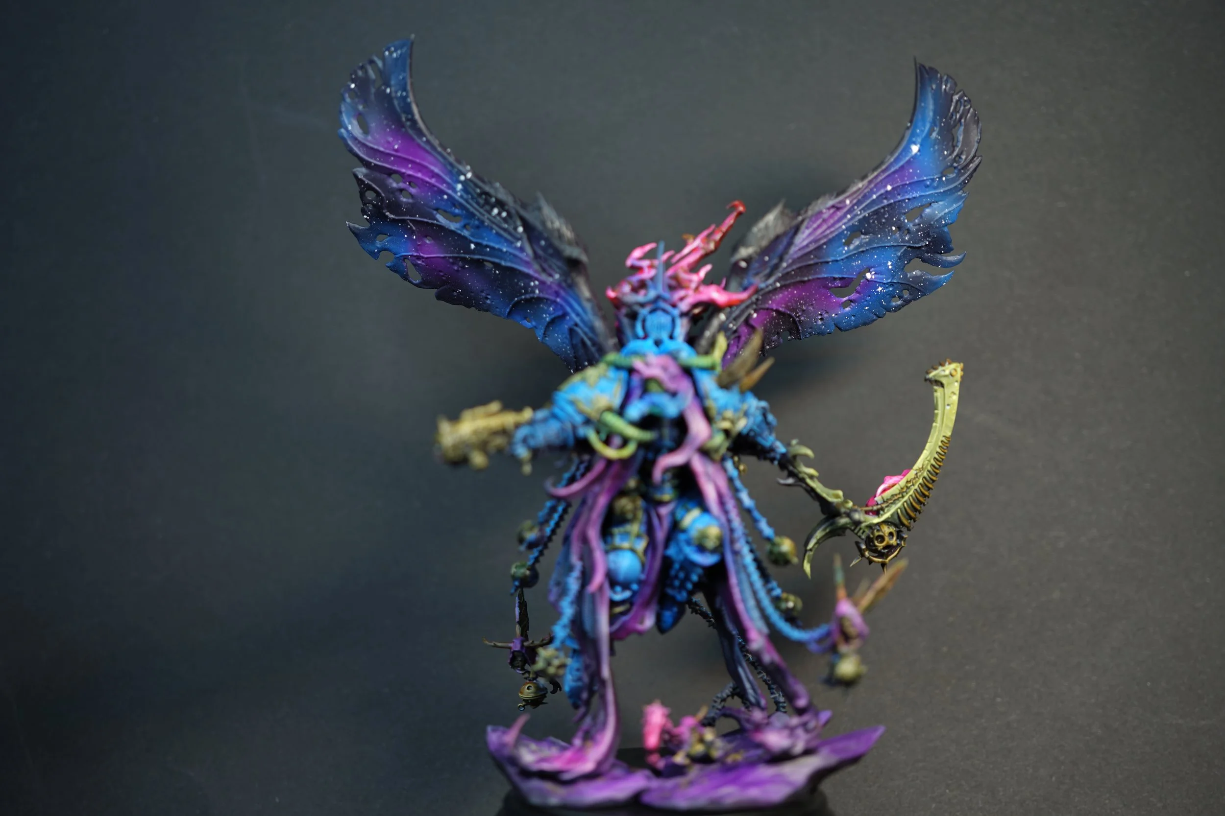 A detailed, colorful figurine of Mortarion from Warhammer 40k with large wings, multiple tentacle-like appendages, and a large scythe in one hand, against a dark background.