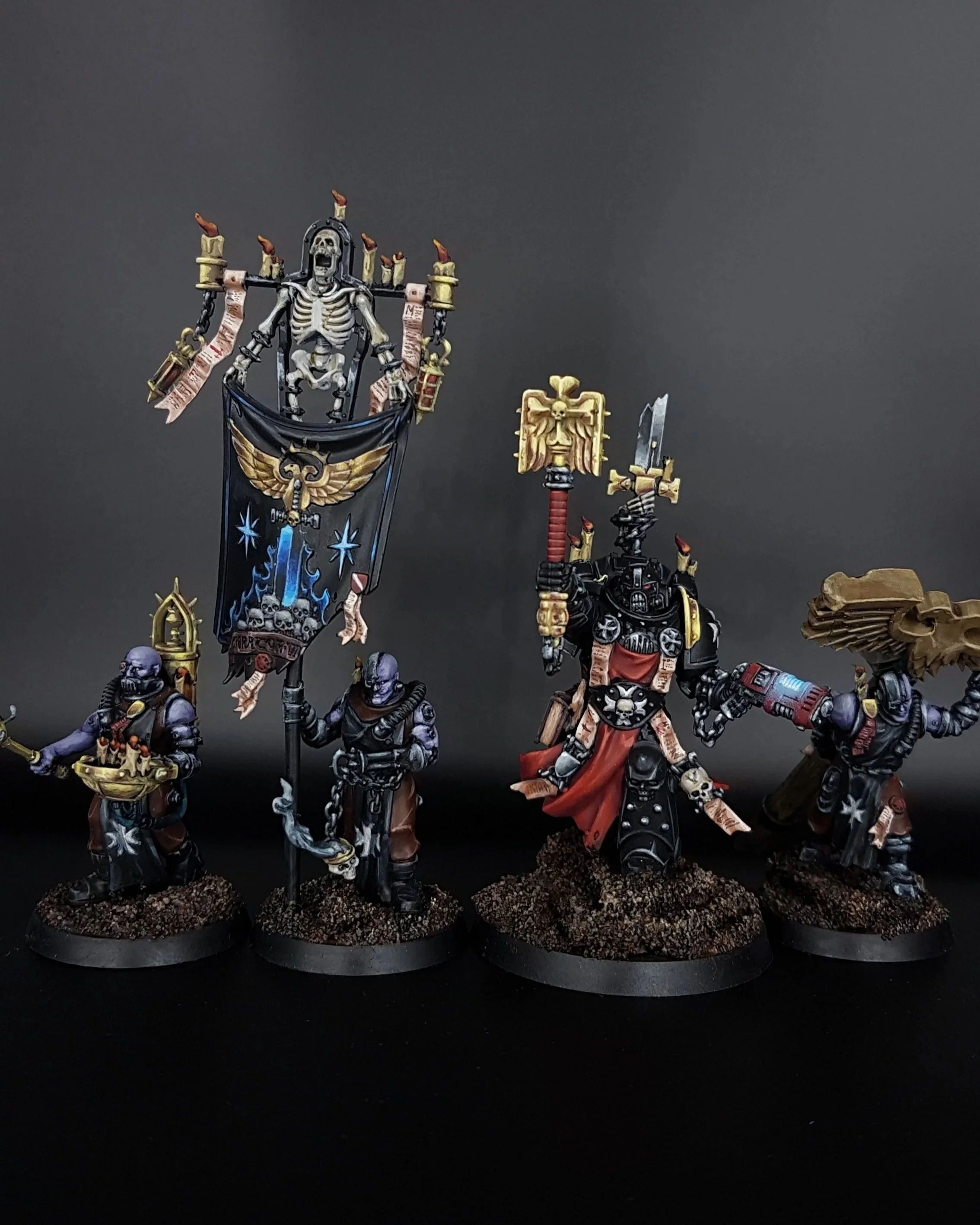 Four intricately painted Black Templar miniature figures in dark armor from Warhammer 40k, with one holding a banner depicting a skeleton, and another wielding a large sword, placed on textured bases against a black background.