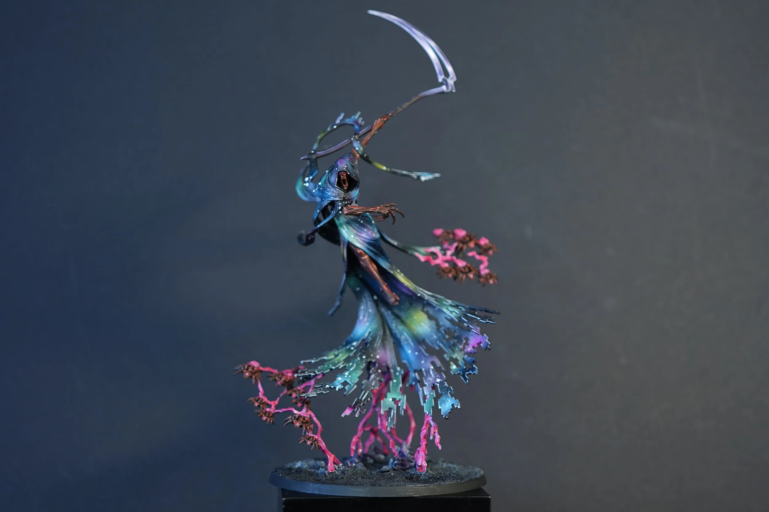 A detailed painted miniature figure of a Nightbringer C'Tan shard from the Warhammer 40k Necrons painted with a galaxy nebula cloak and a large scythe, standing on a textured base with pink energy branches against a plain dark background.