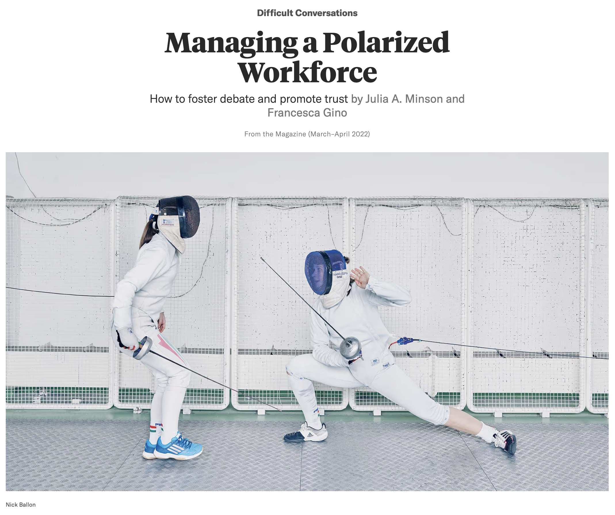 Two fencers in white gear; one in a lunge position, the other preparing to defend, behind a white fencing screen.