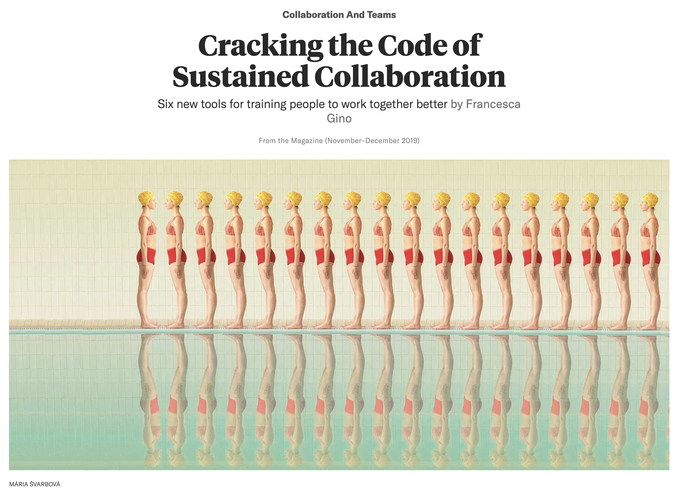 A line of women in swimsuits with yellow swim caps standing at the edge of a swimming pool, their reflections visible in the water.