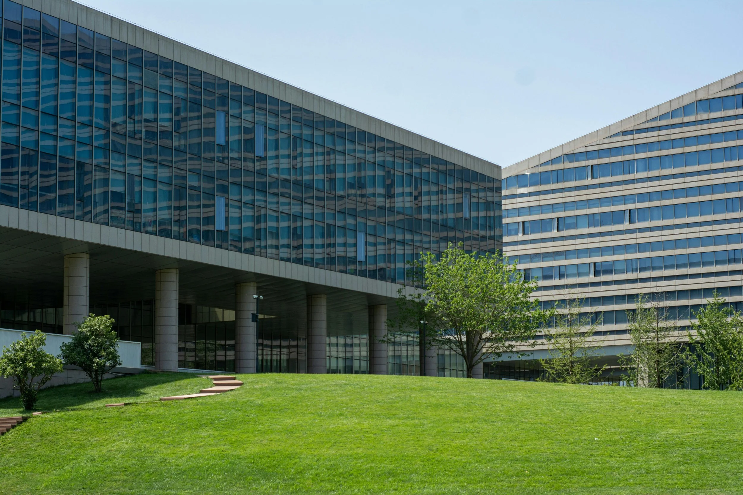 Modern office building with glass windows on a sunny day, surrounded by a well-maintained green lawn and trees.