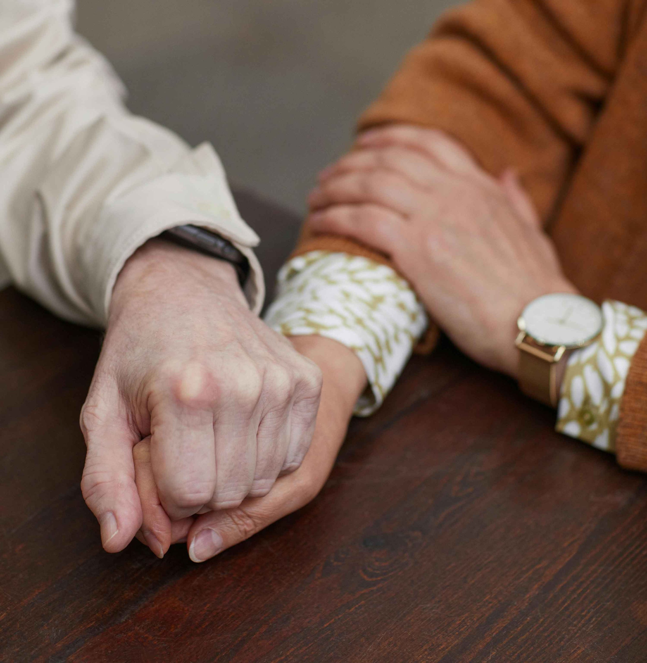 Two elderly people holding hands on a wooden table.